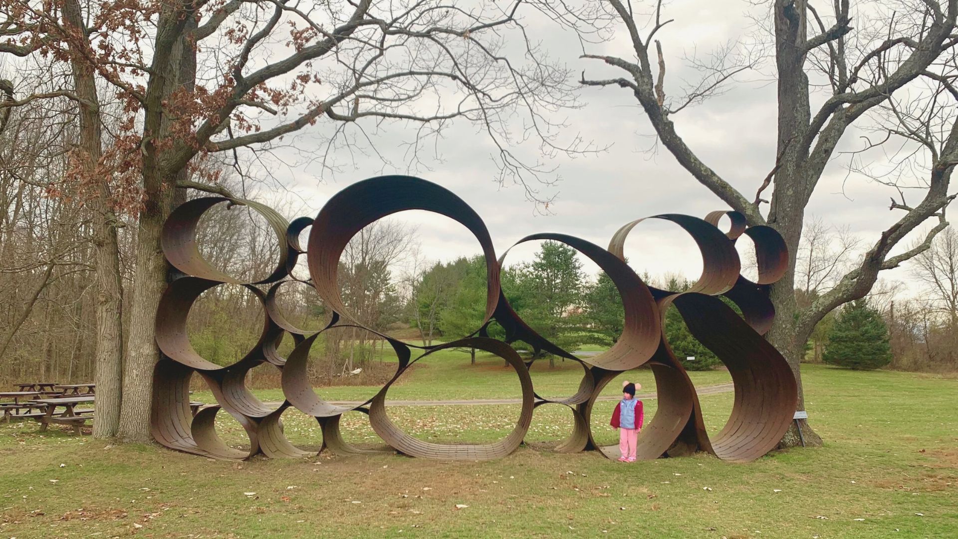 A woman stands beside a large metal sculpture, showcasing her admiration for the intricate design and craftsmanship.