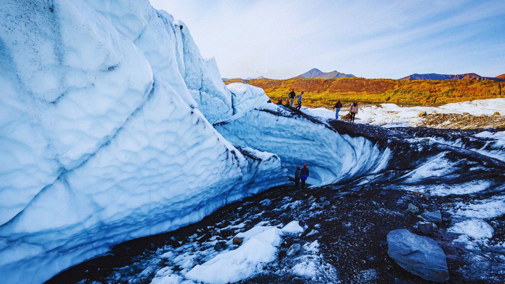 . People walking through a stunning ice cave surrounded by towering mountain walls.