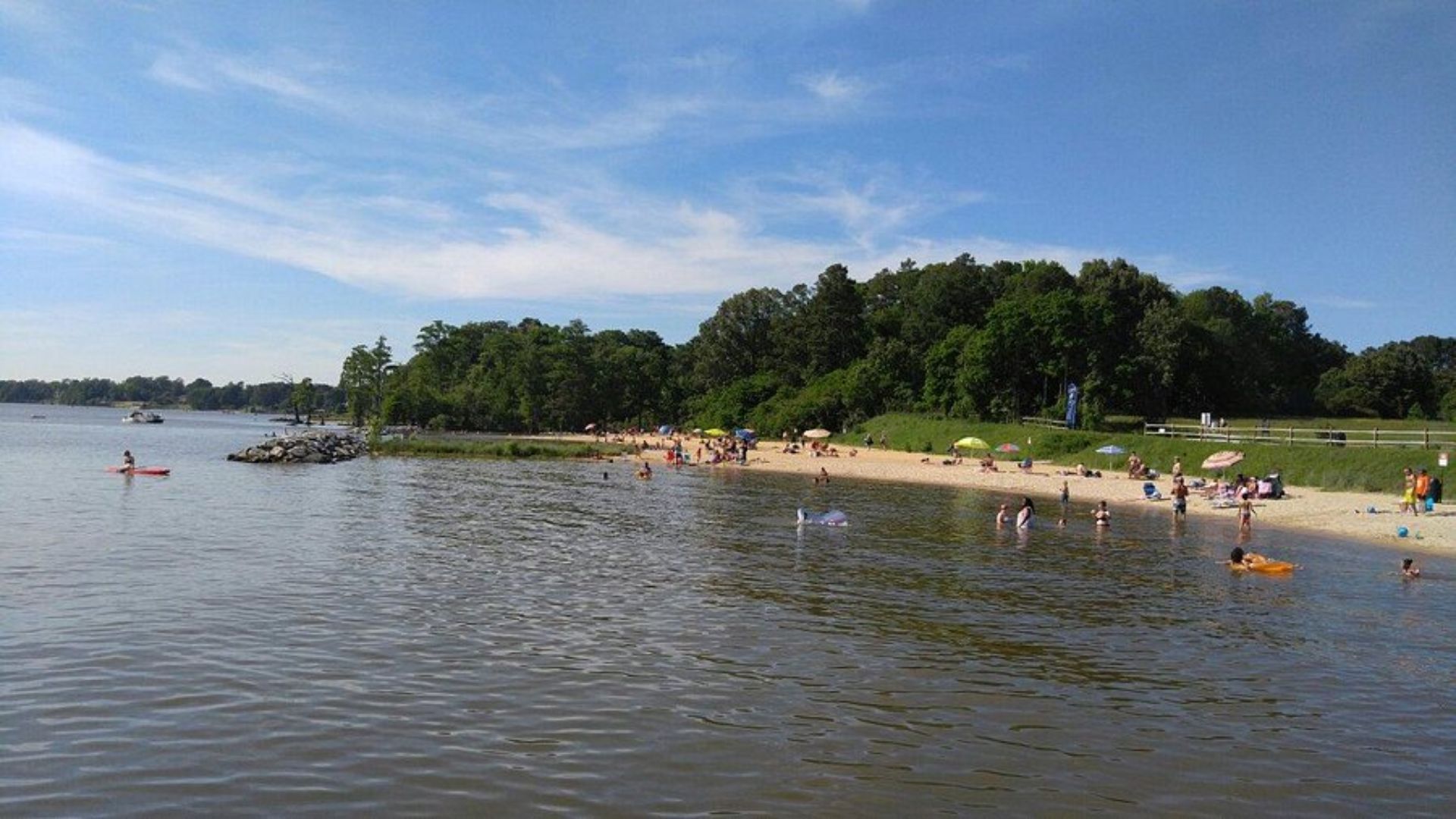 A sunny beach scene with people swimming in the water and sunbathing on the sand.