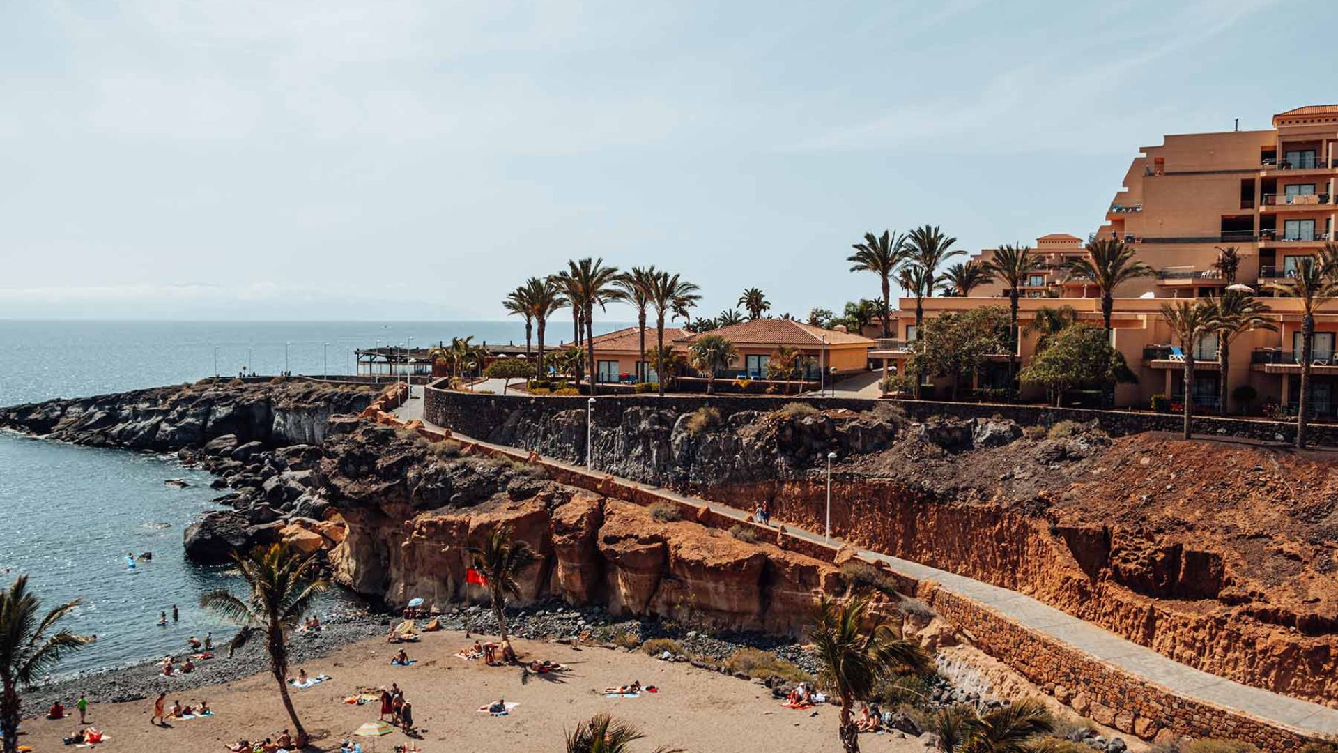 A scenic beach featuring palm trees with a hotel situated alongside the shoreline.