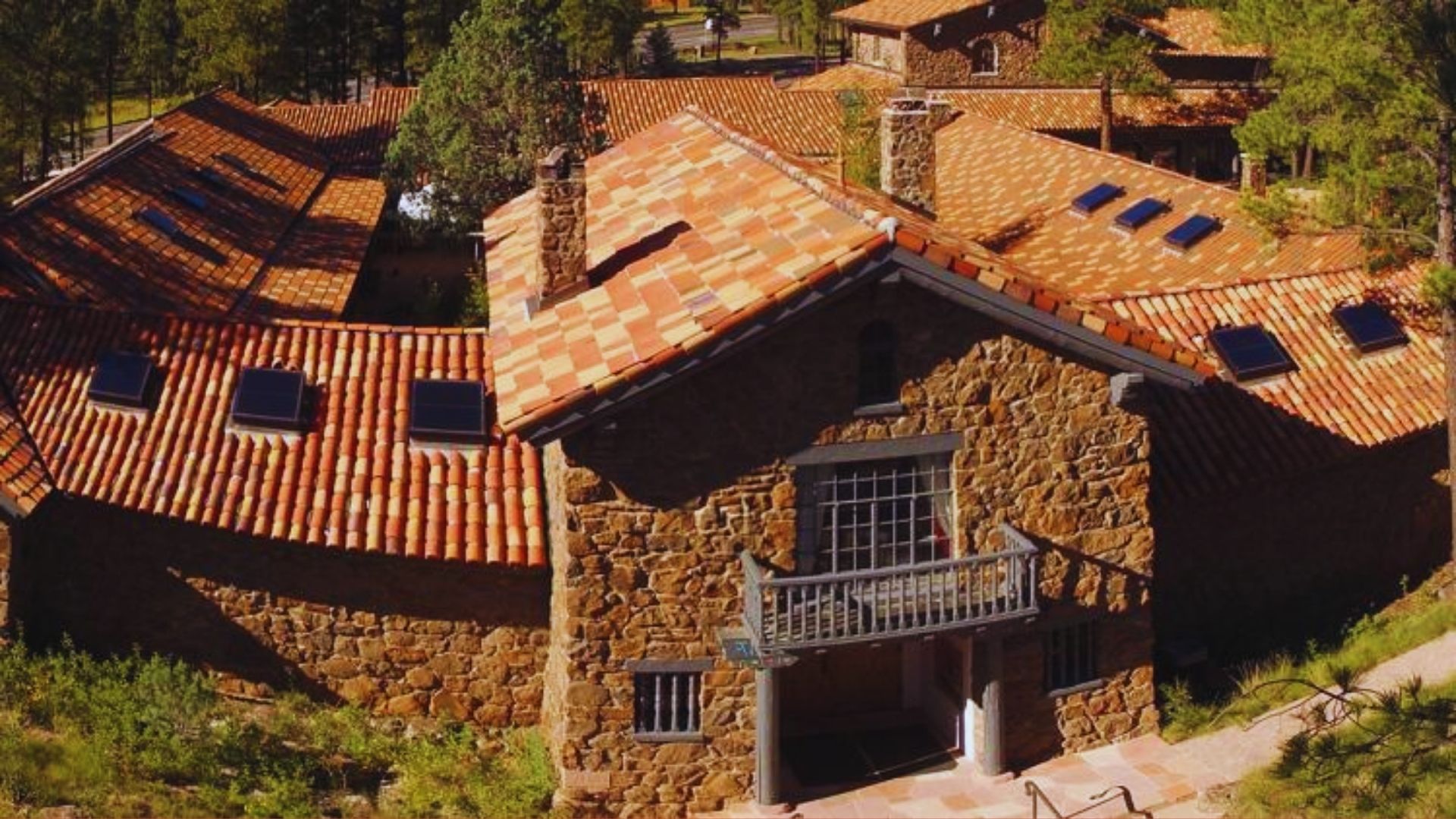 Aerial view of a stone building featuring a red tile roof, surrounded by greenery and other structures.