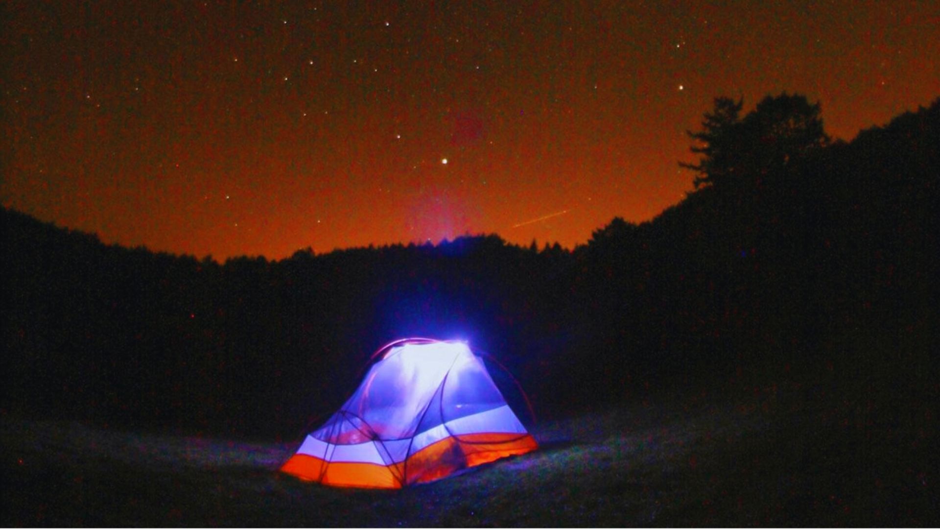 A brightly lit tent at night under a starry sky, creating a serene and inviting atmosphere.
