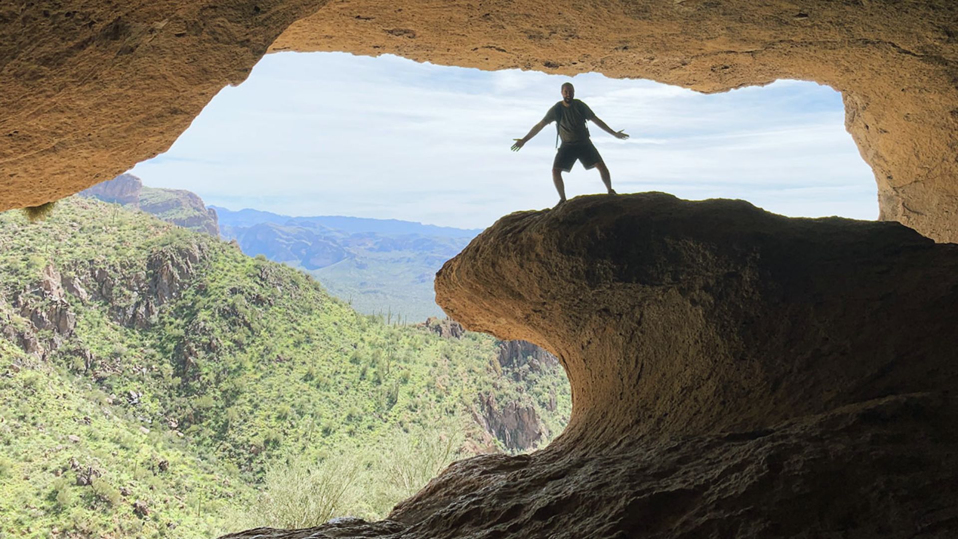 A man stands in the center of a dimly lit cave, surrounded by rocky walls and shadows.