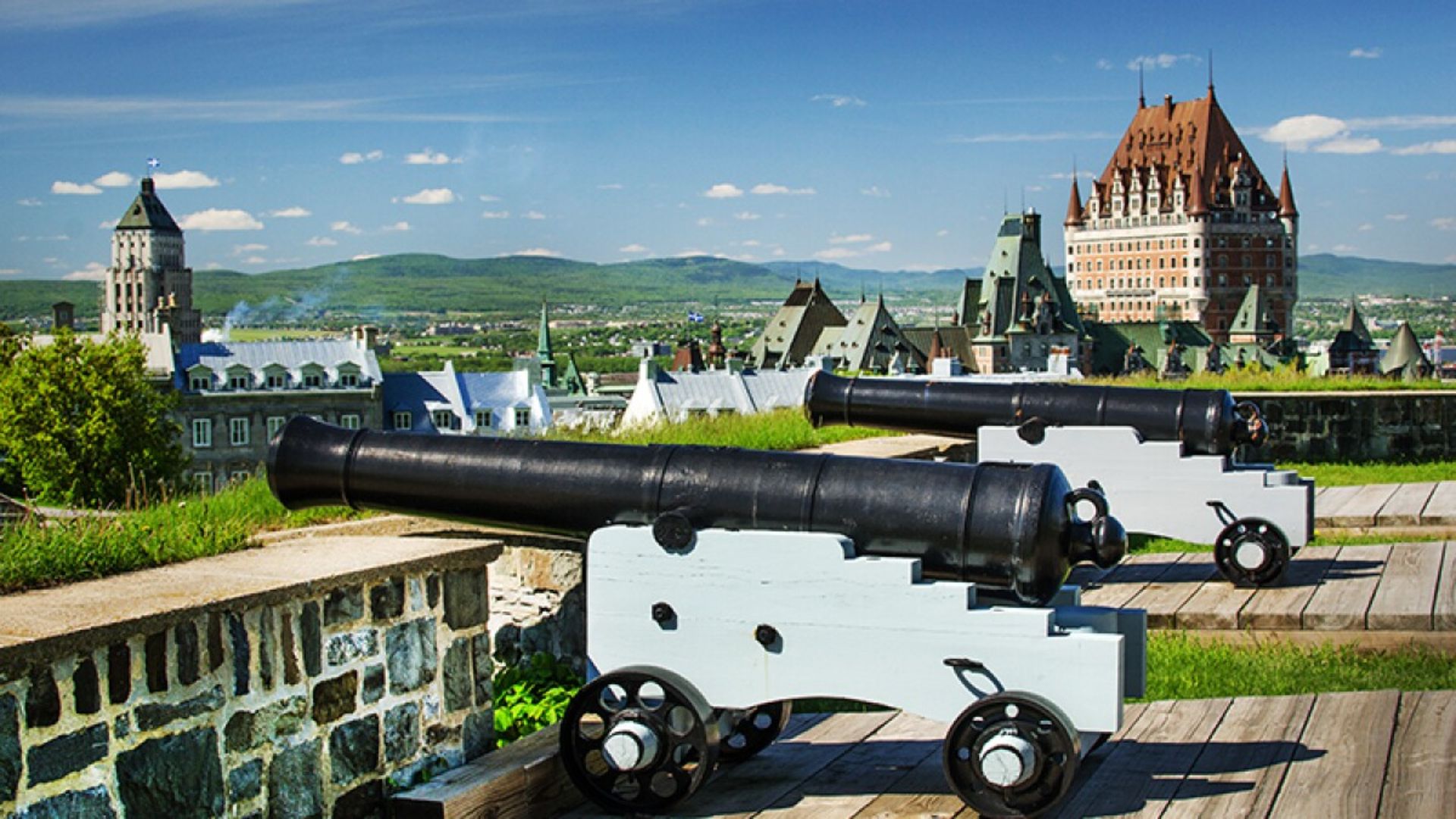 Two cannons positioned on a wooden platform, overlooking a cityscape in the background.