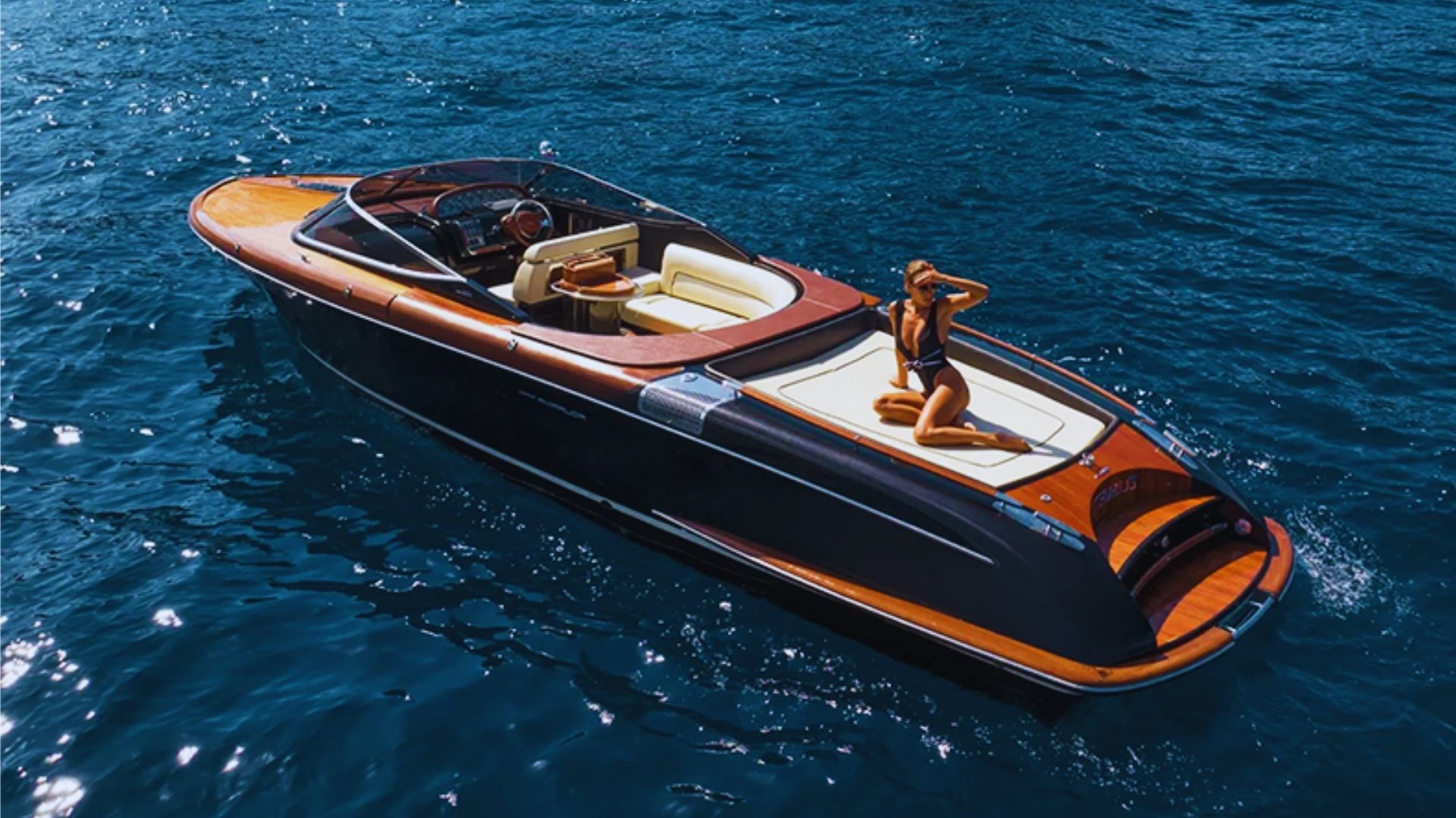 A speedboat carrying two people glides across the water under a clear blue sky.