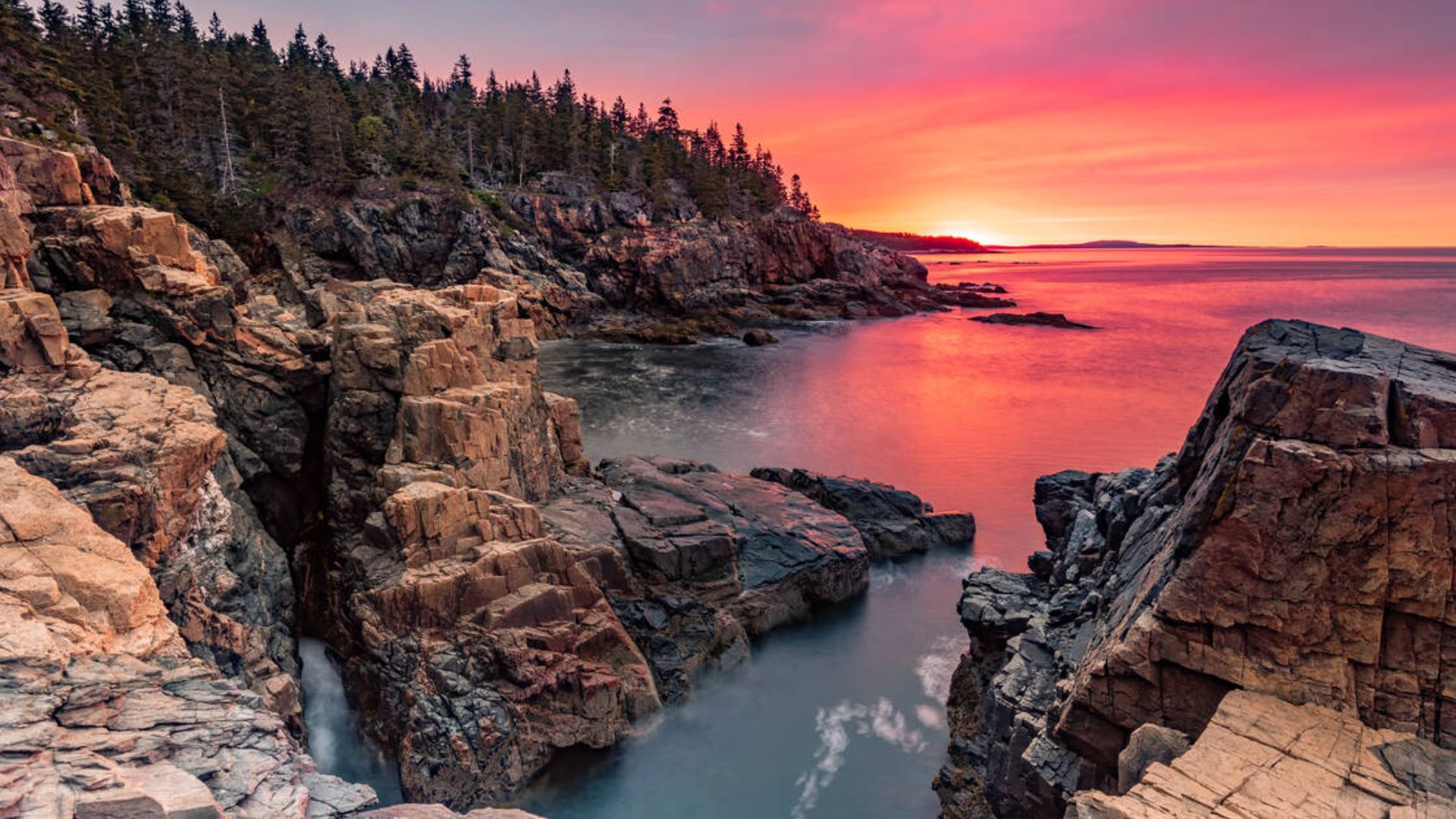 Sunset over Acadia National Park, Maine, showcasing vibrant orange and pink hues against a tranquil landscape.