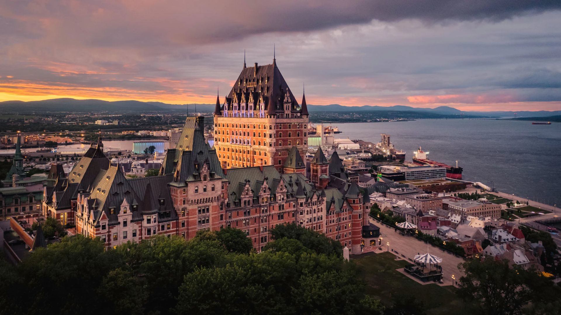 The city of Quebec skyline illuminated by a warm sunset, casting vibrant colors over historic buildings and the St. Lawrence River.