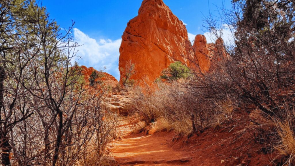 A winding trail leads toward a striking red rock formation under a clear blue sky.