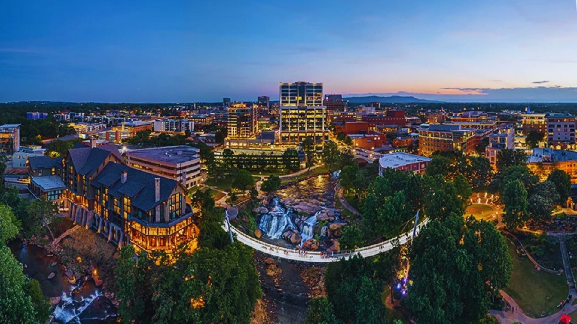 Greenville, SC skyline at dusk, showcasing illuminated buildings against a colorful twilight sky.