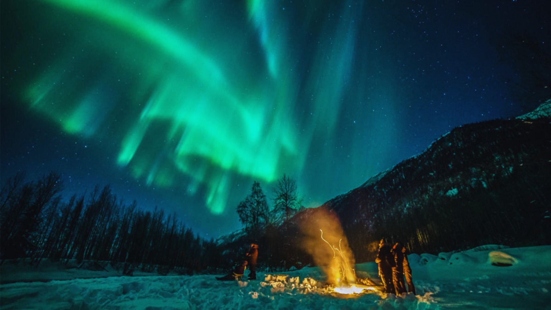 Aurora borealis illuminates the night sky above a campfire in Alaska, creating a stunning natural spectacle.