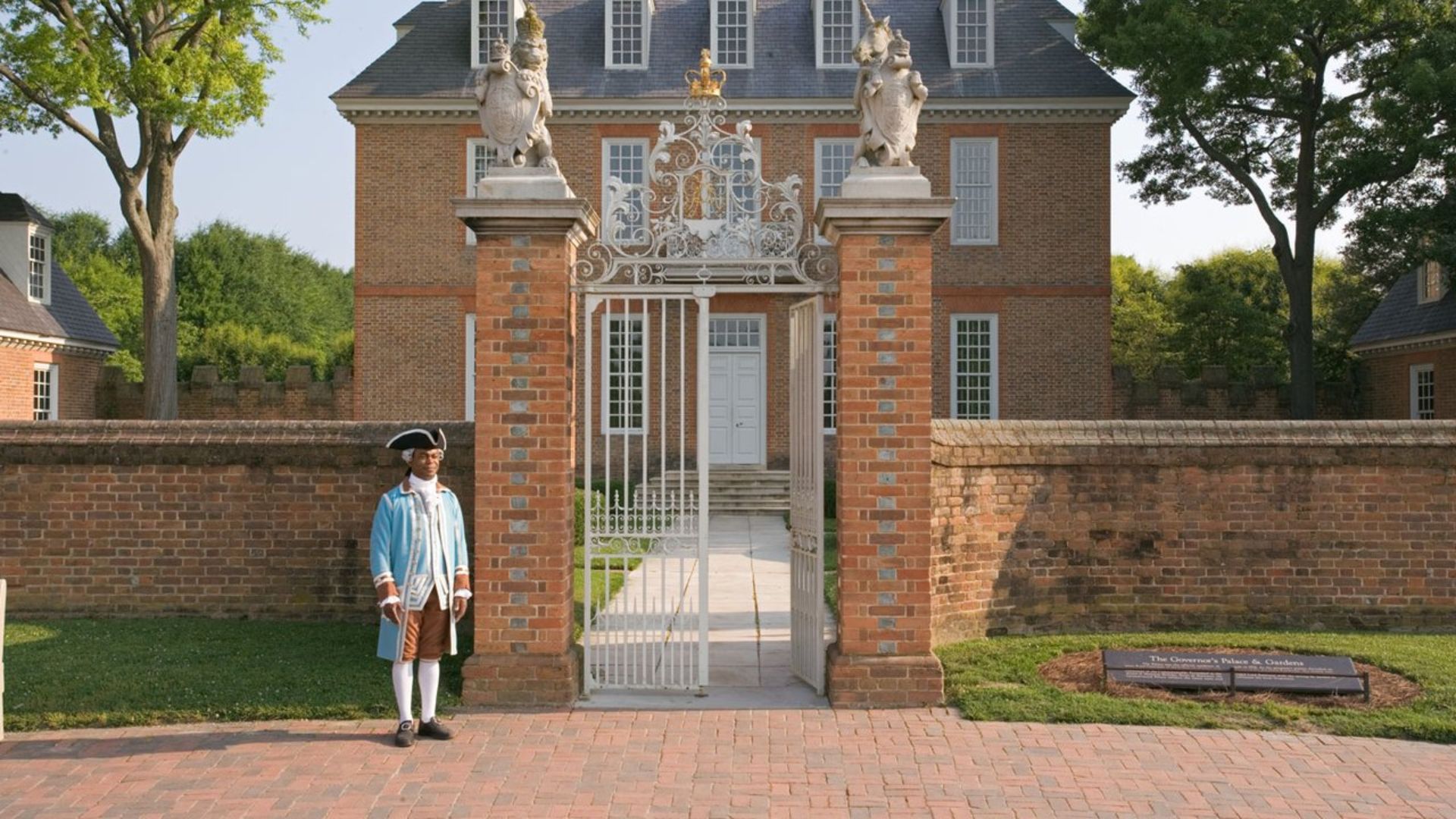 A man in a blue uniform stands confidently in front of a brick building.