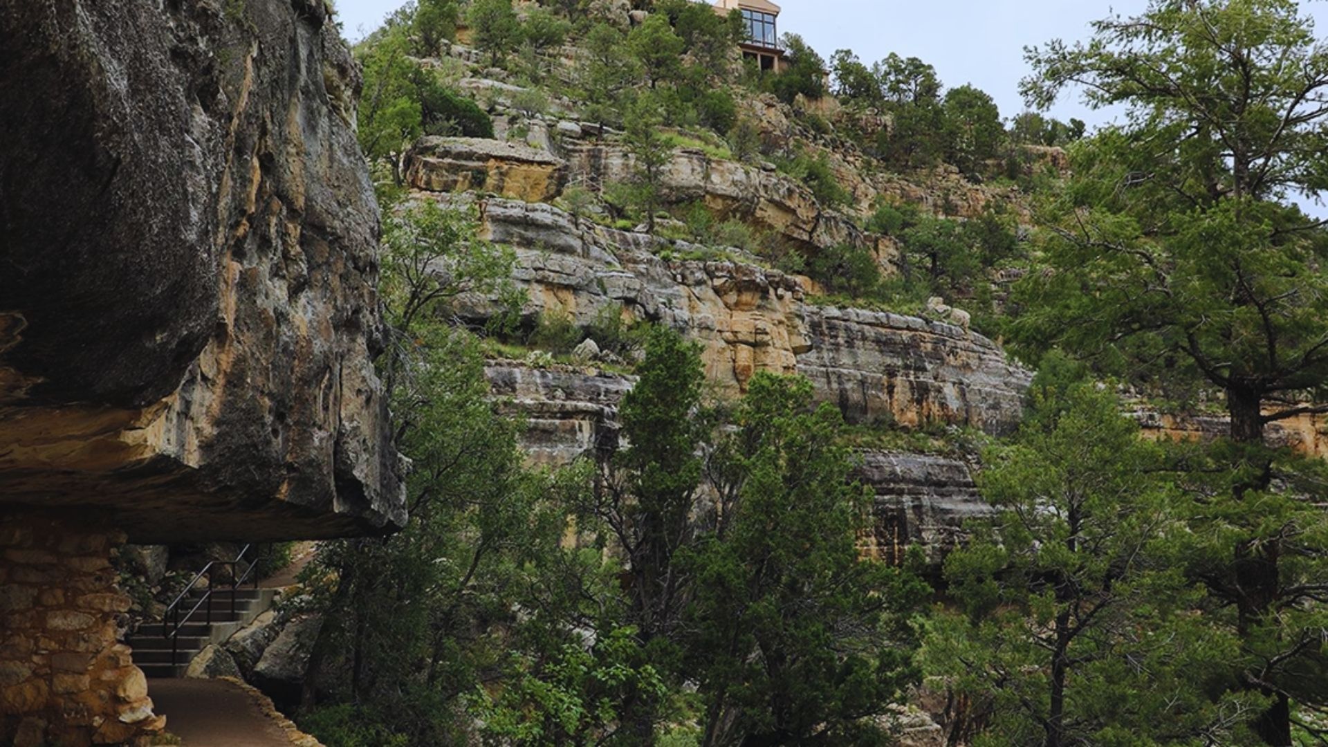 A scenic path ascends a cliff, leading to a building situated on the summit, with a backdrop of sky and landscape.