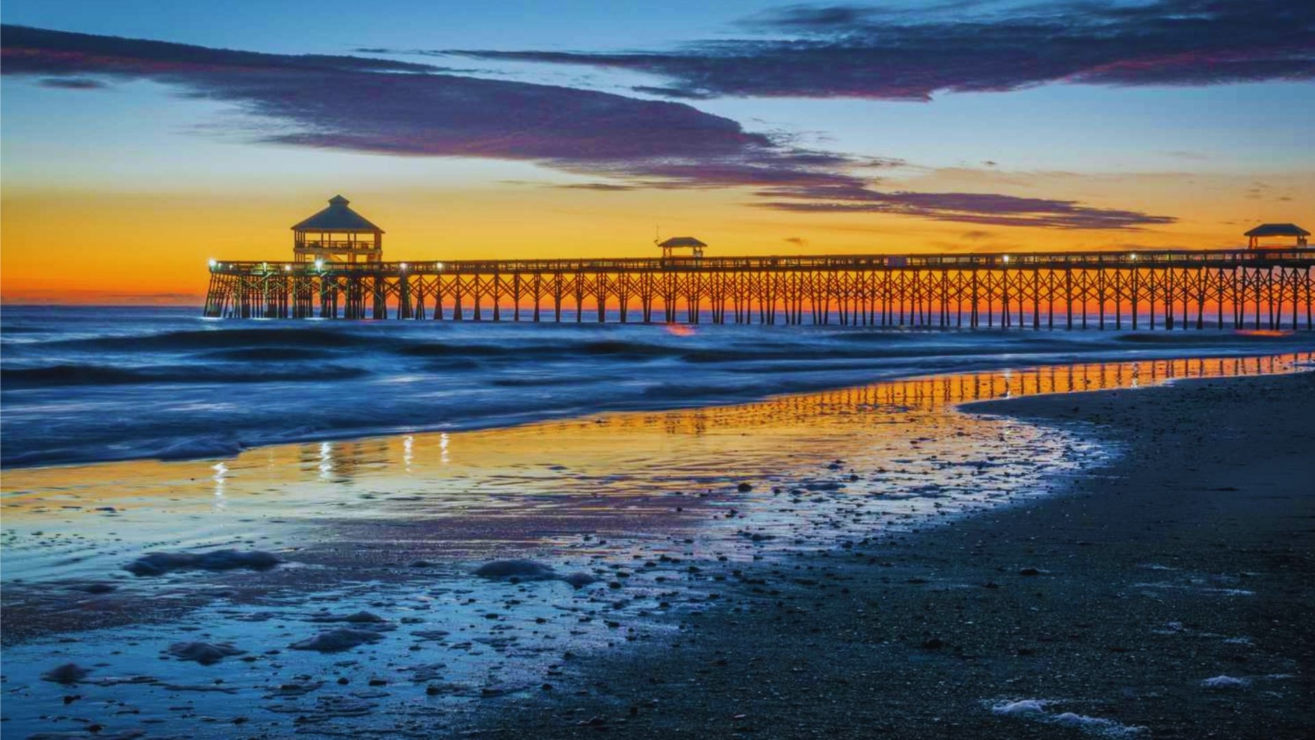 Sunset over the pier at Myrtle Beach, SC, with vibrant orange and purple hues reflecting on the water.