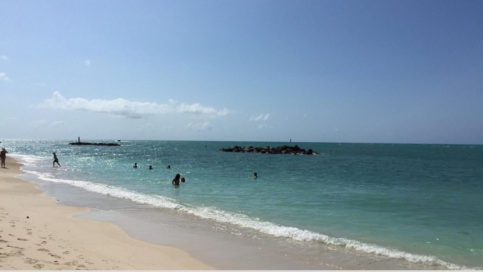 People swimming in the ocean at a sunny beach, enjoying the warm weather and clear blue water.