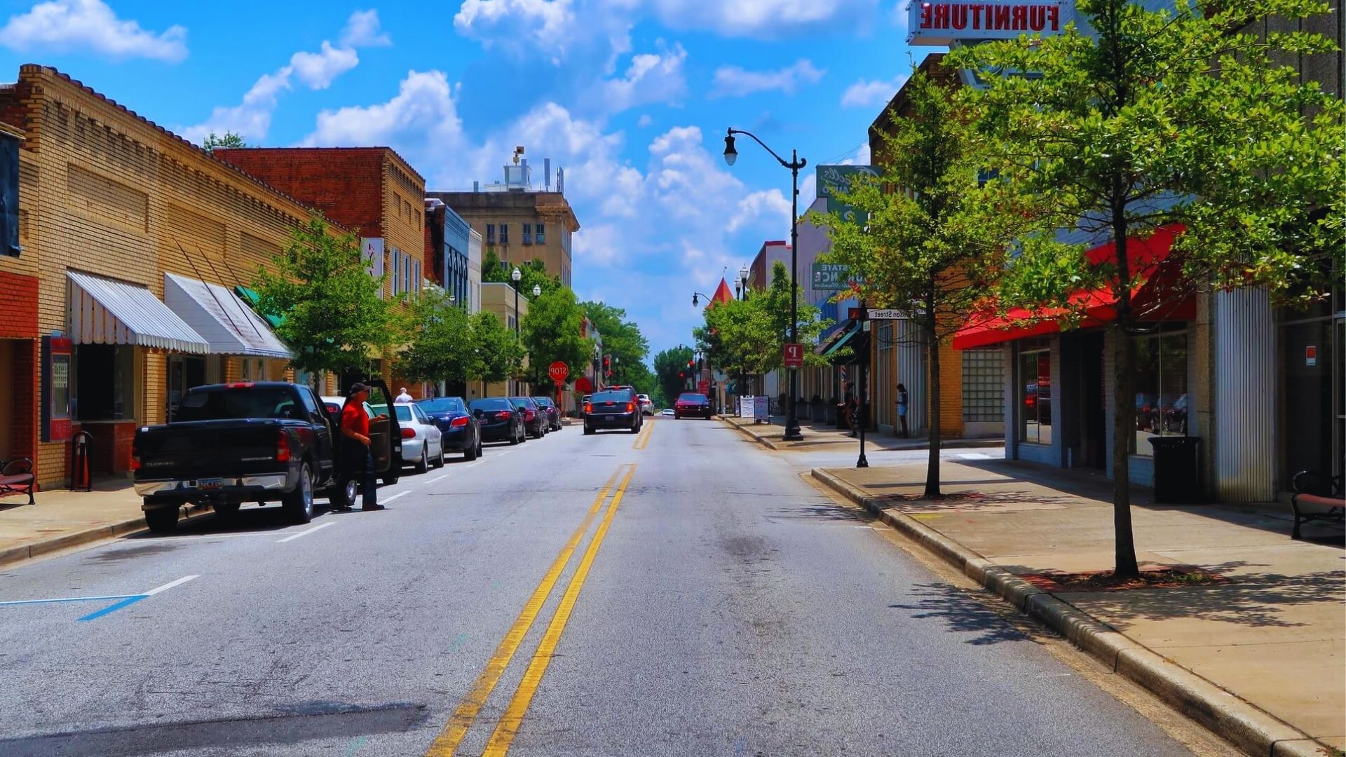 A city street lined with parked cars on both sides, showcasing urban life and traffic patterns.