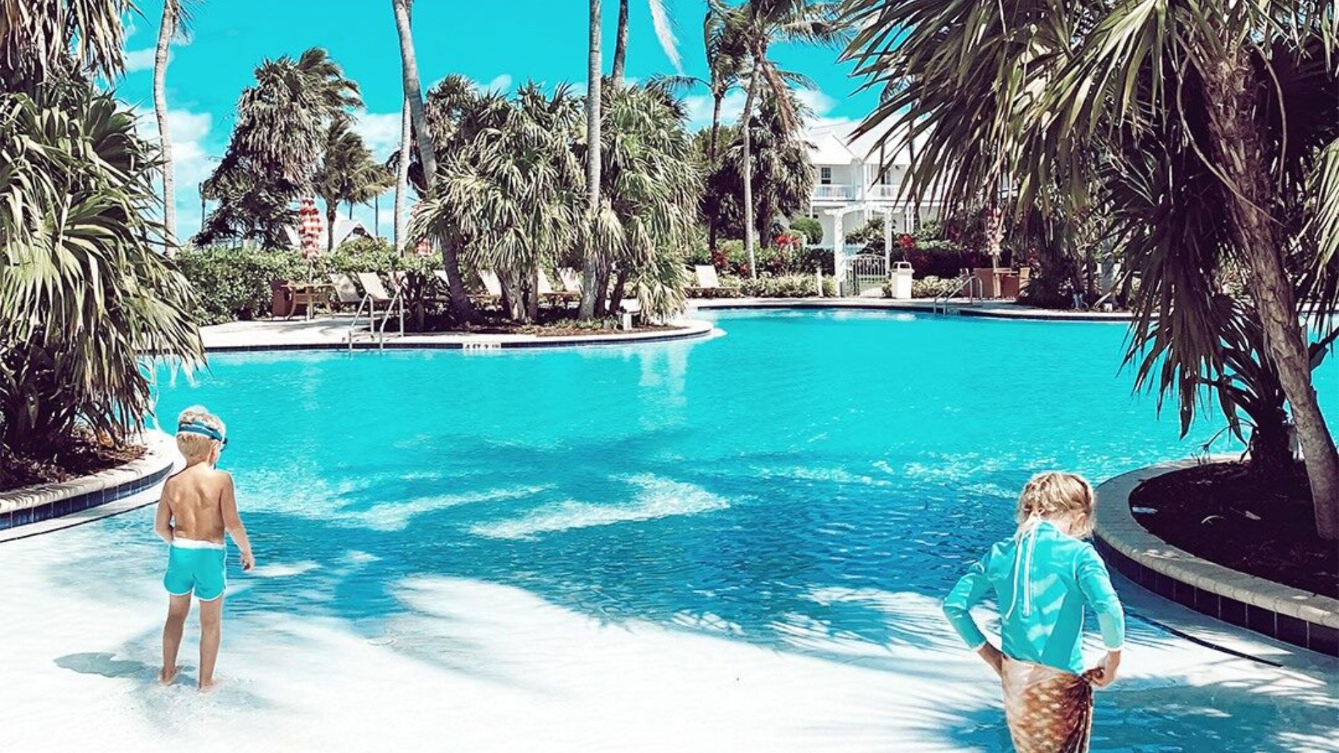 Two children stand in a resort pool, enjoying the water and sunshine together.