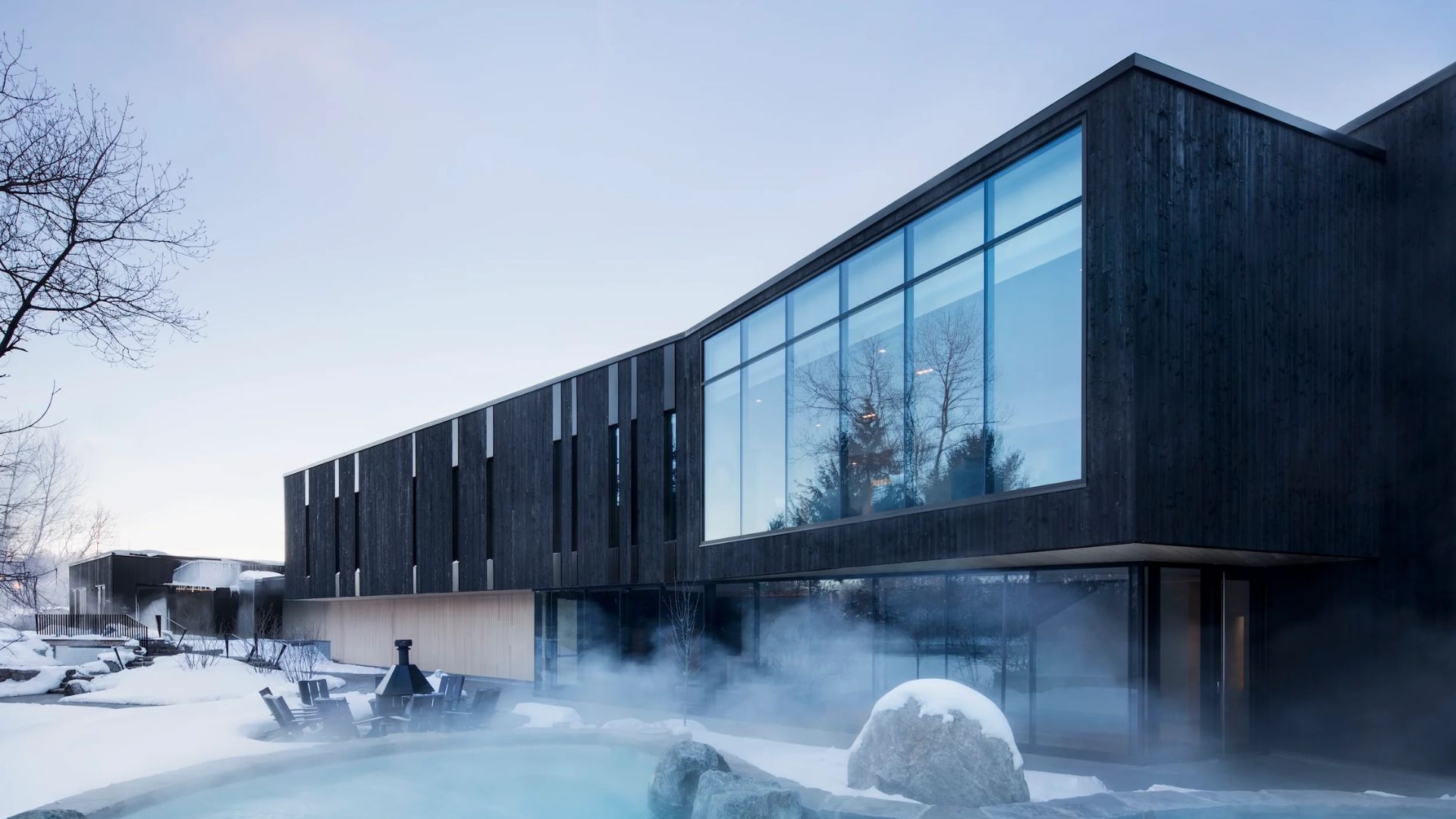 A modern building featuring a hot tub surrounded by snow, showcasing a cozy winter retreat atmosphere.