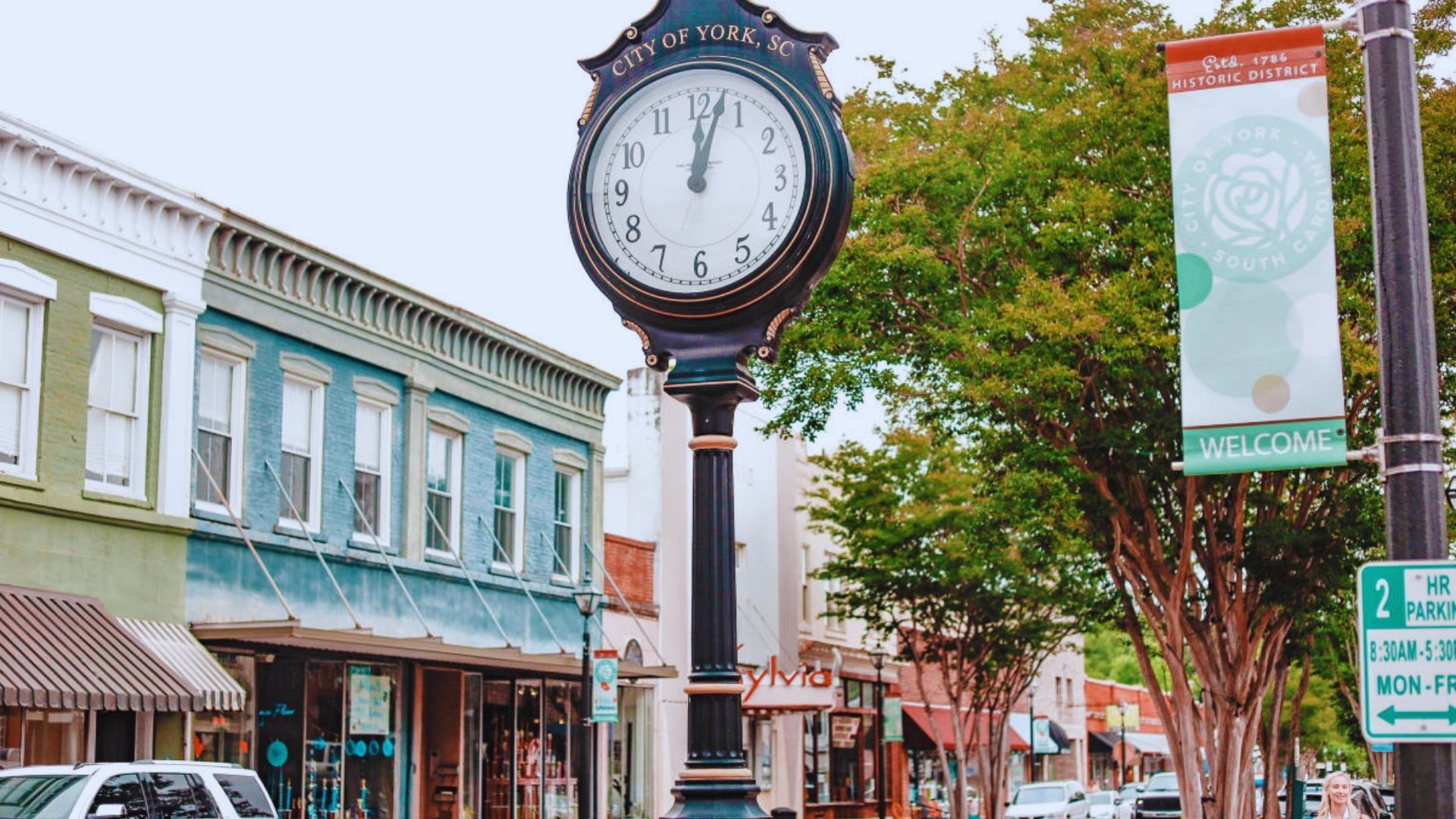 A street clock mounted on a pole, displaying the time in a bustling city environment.