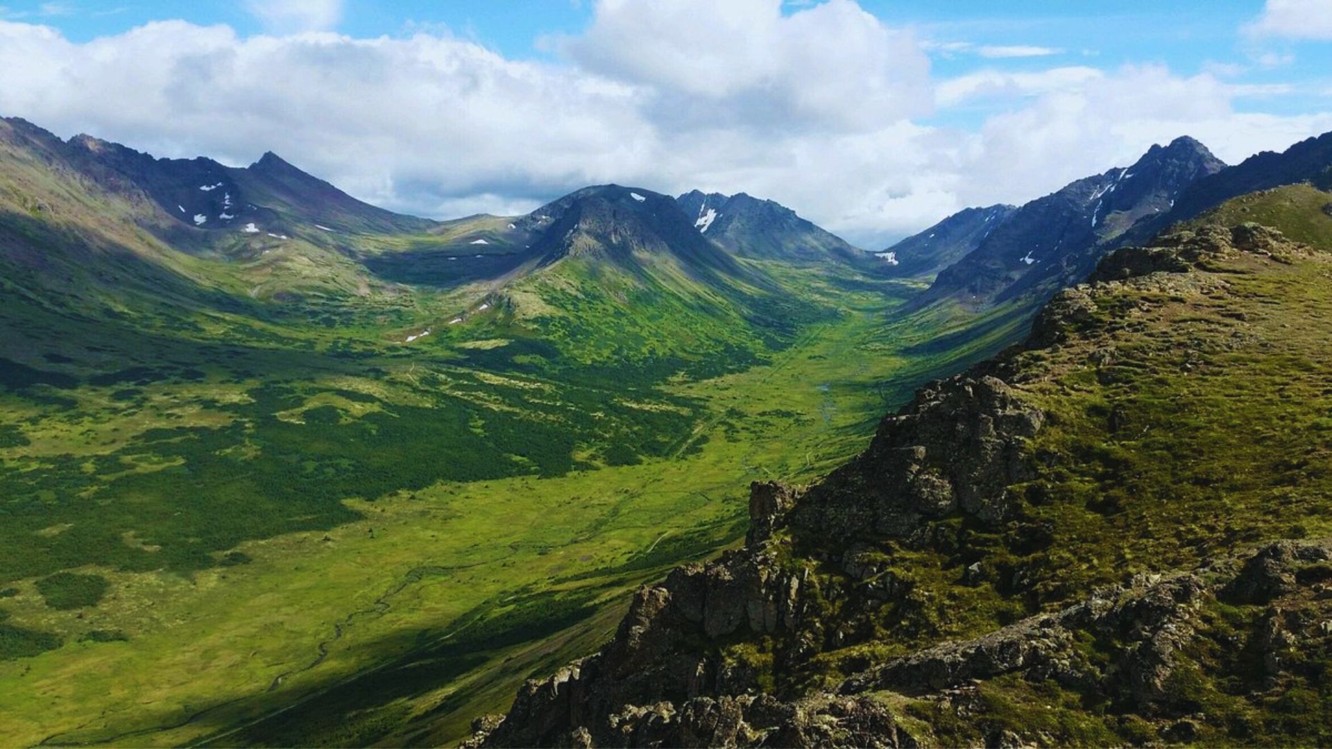Panoramic view of mountains and valleys from a mountain summit, showcasing lush greenery and rugged terrain below.