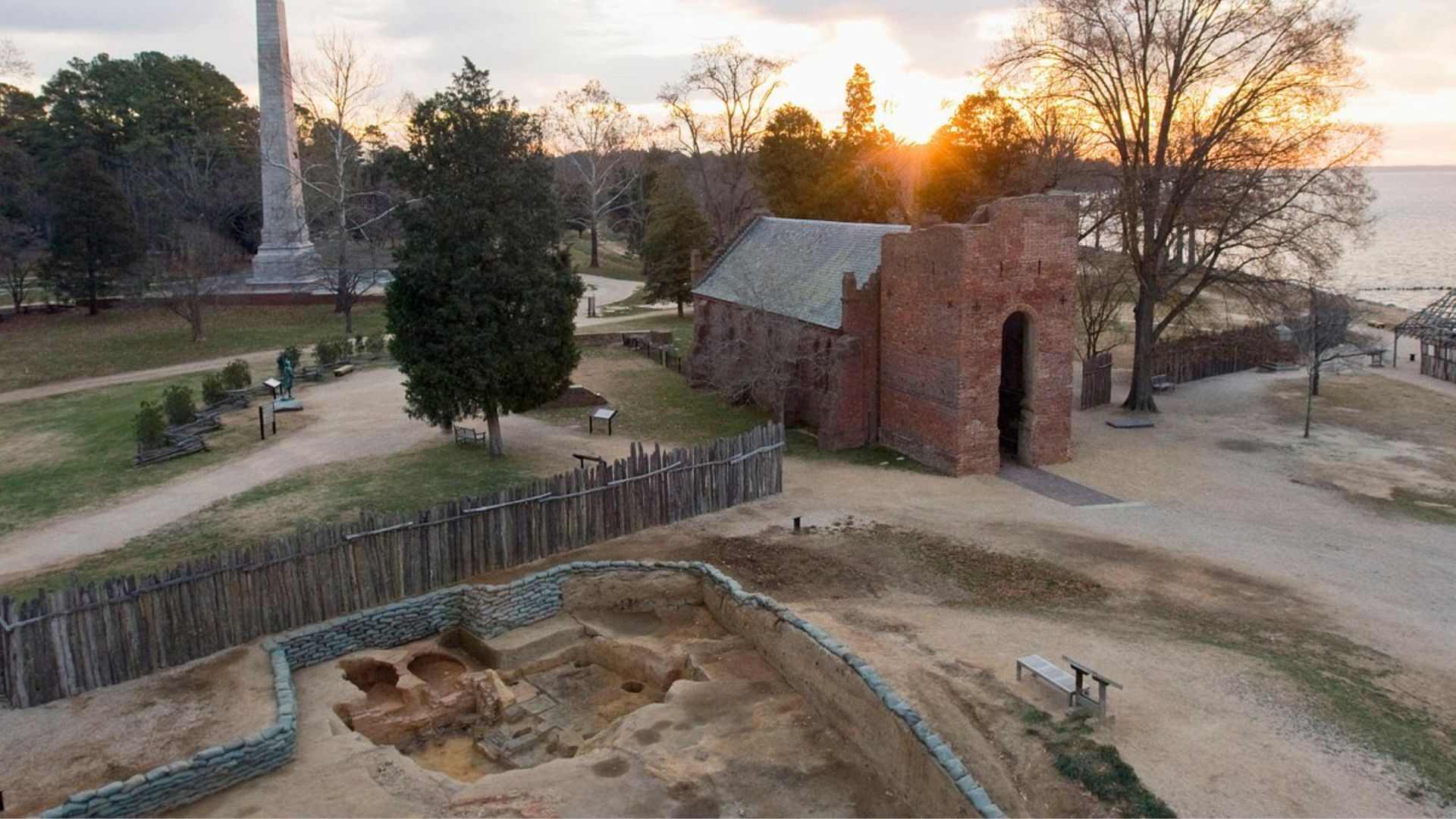 The sun sets behind the ruins of a church and a monument, casting warm hues over the historic landscape.