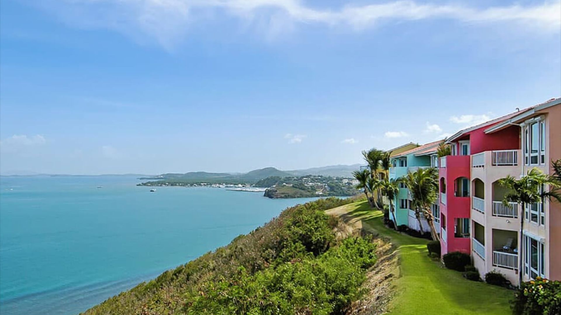 A vibrant building stands by the ocean, with a sandy beach stretching out beneath a clear blue sky.