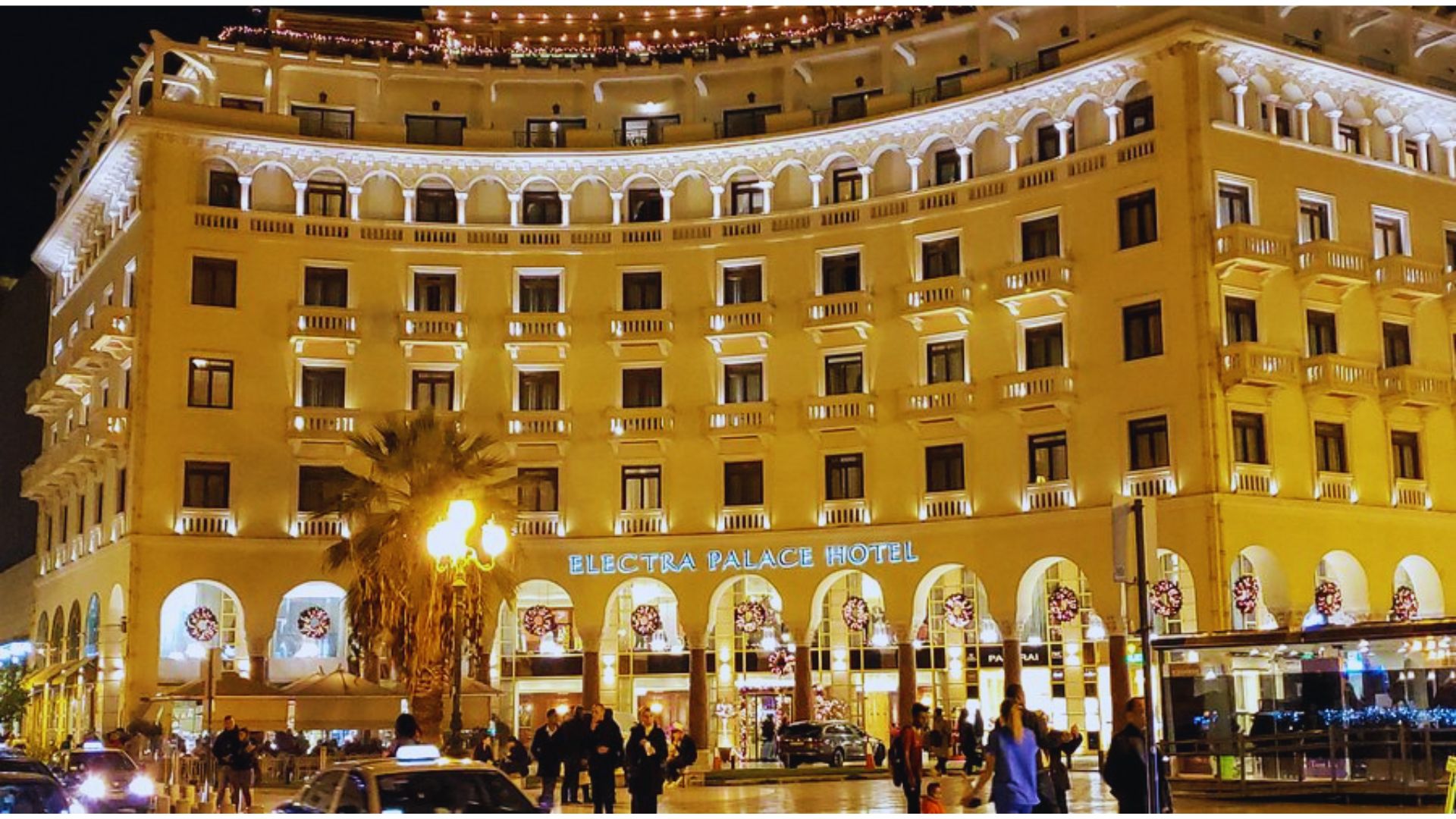 The hotel illuminated at night, with people strolling around the vibrant outdoor area.