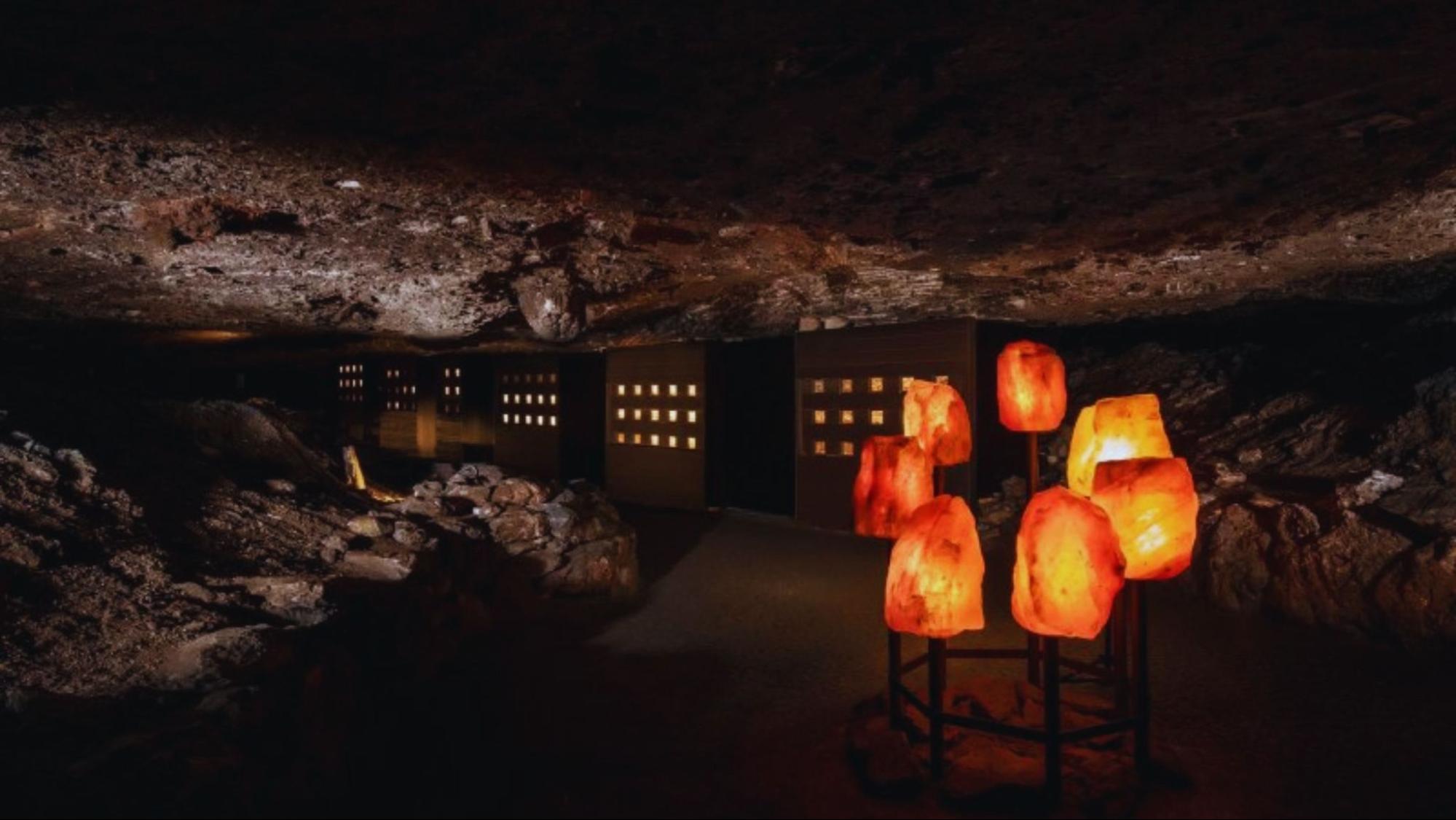 A dimly lit cave featuring decorative lamps and a rugged rock wall, creating an atmospheric underground scene.
