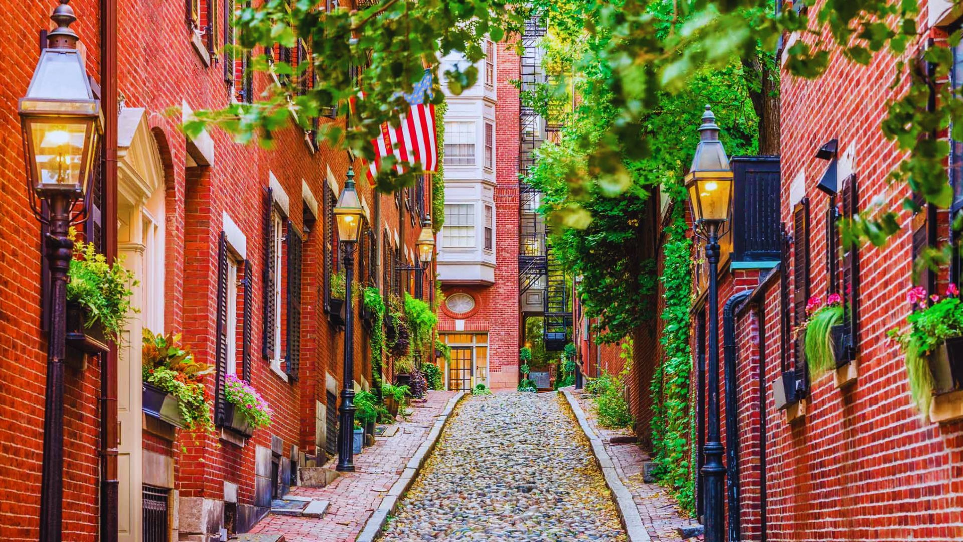 A narrow cobblestone street in Boston, Massachusetts, lined with historic buildings and vibrant greenery.