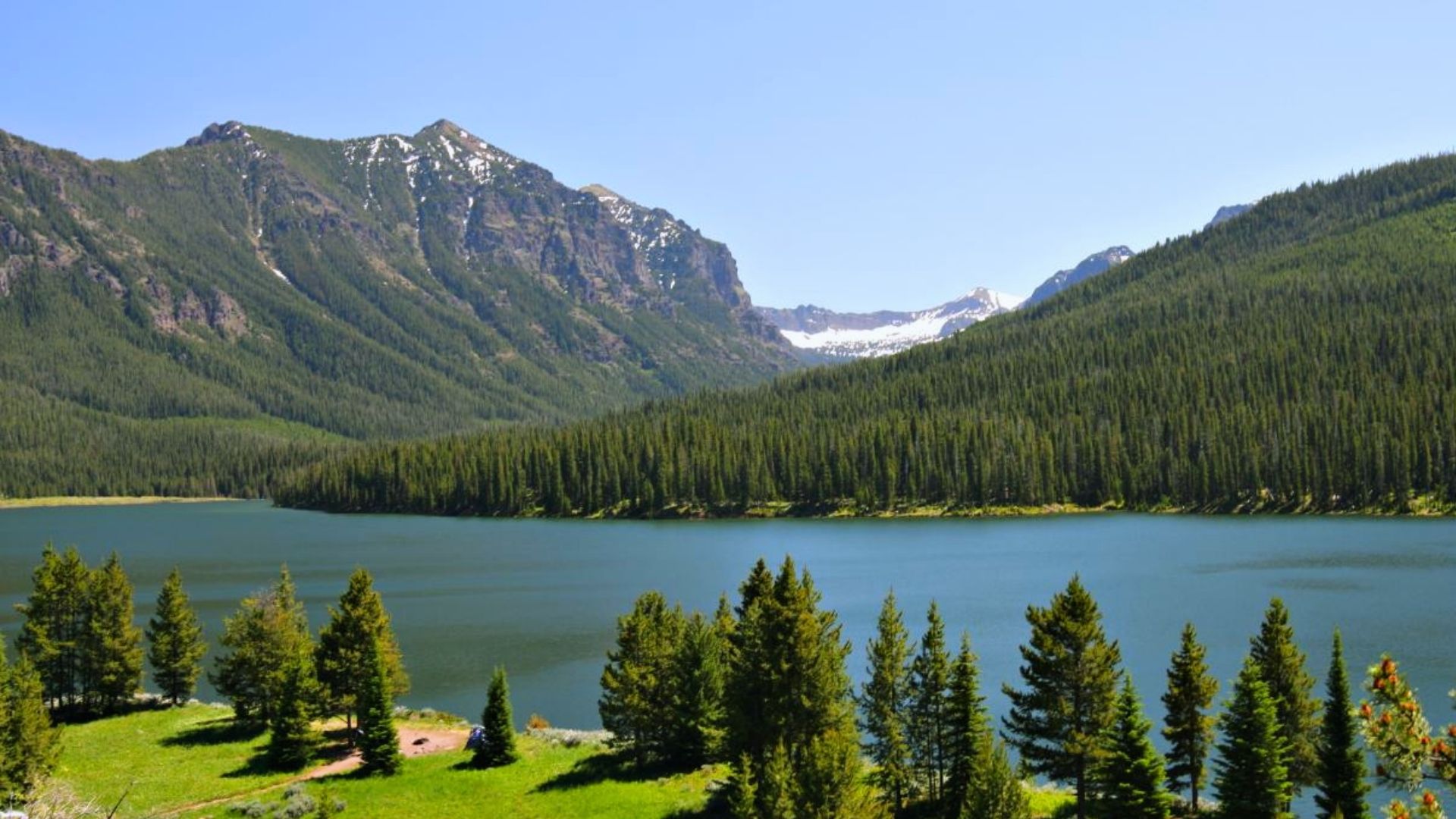 A picturesque lake surrounded by rugged mountains and vibrant trees, showcasing a peaceful natural setting.