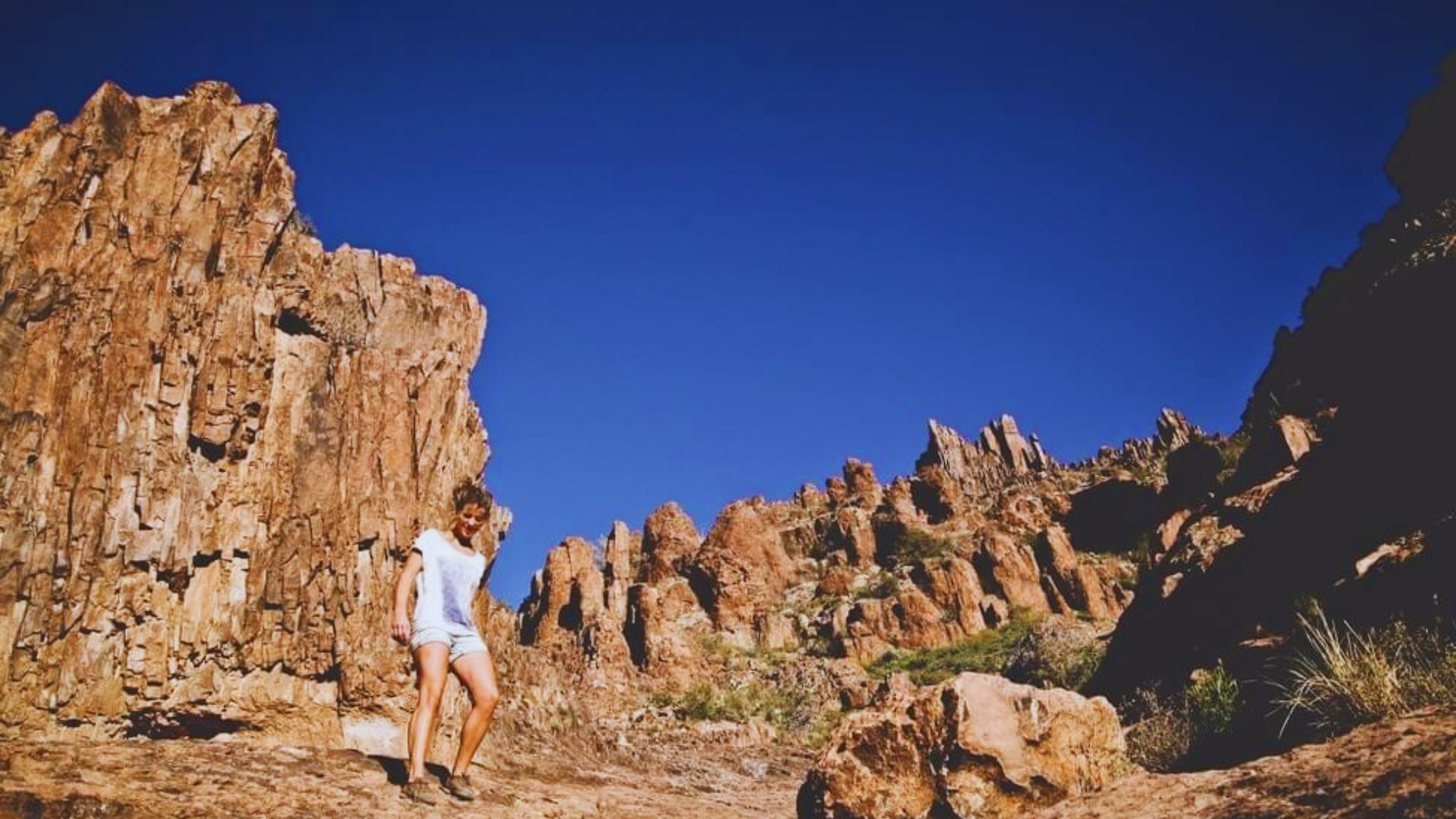 A woman poses in front of large rocks, highlighting her presence in a natural outdoor setting.