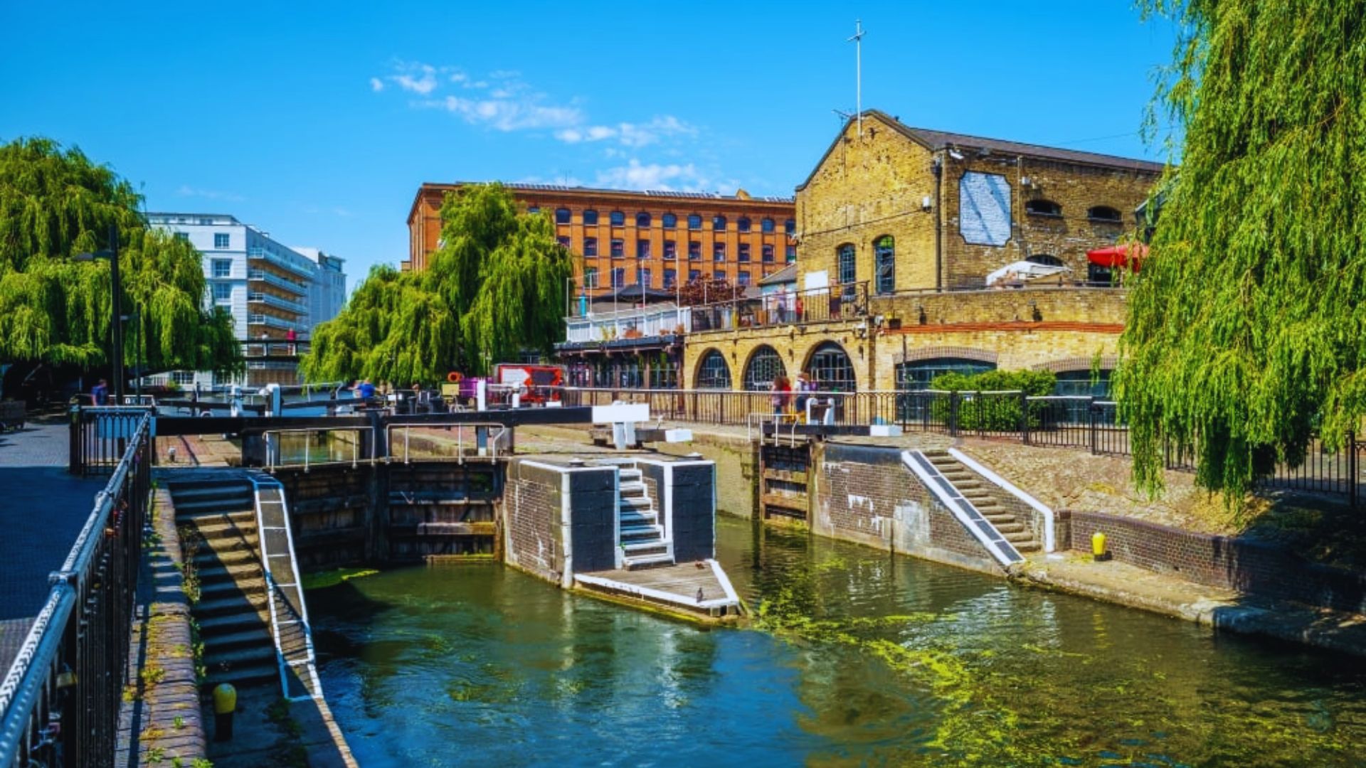 A picturesque London canal scene with a boat passing under a bridge.