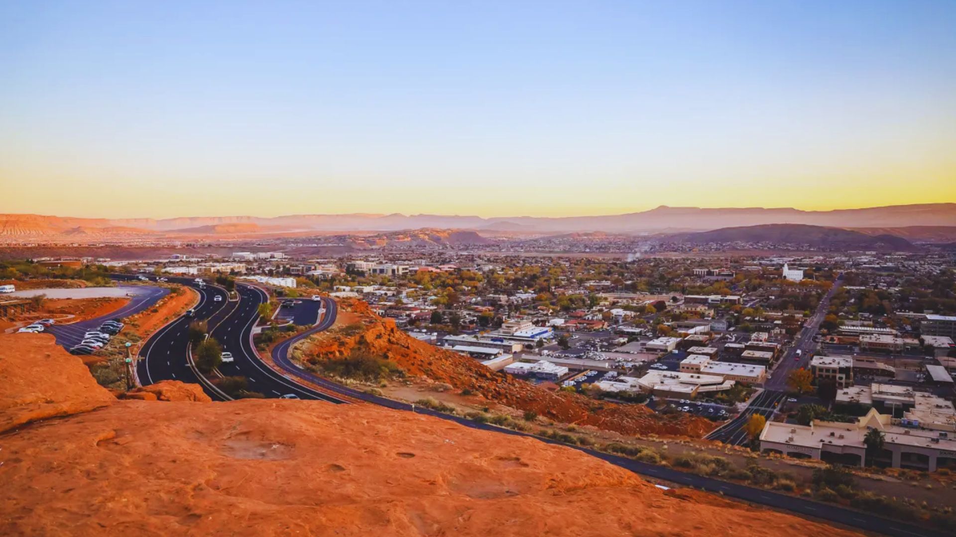 A panoramic view of Utah city at sunset, with vibrant colors illuminating the skyline from a mountain vantage point.