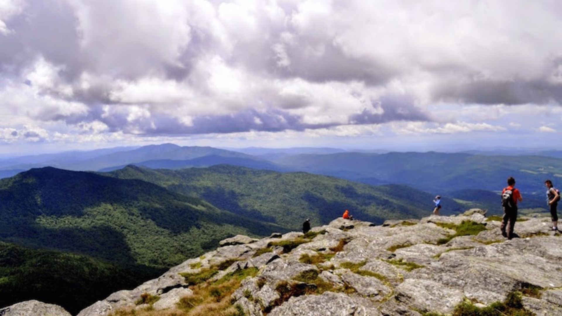 . A group of people standing triumphantly on a mountain peak, surrounded by fluffy clouds in the background.