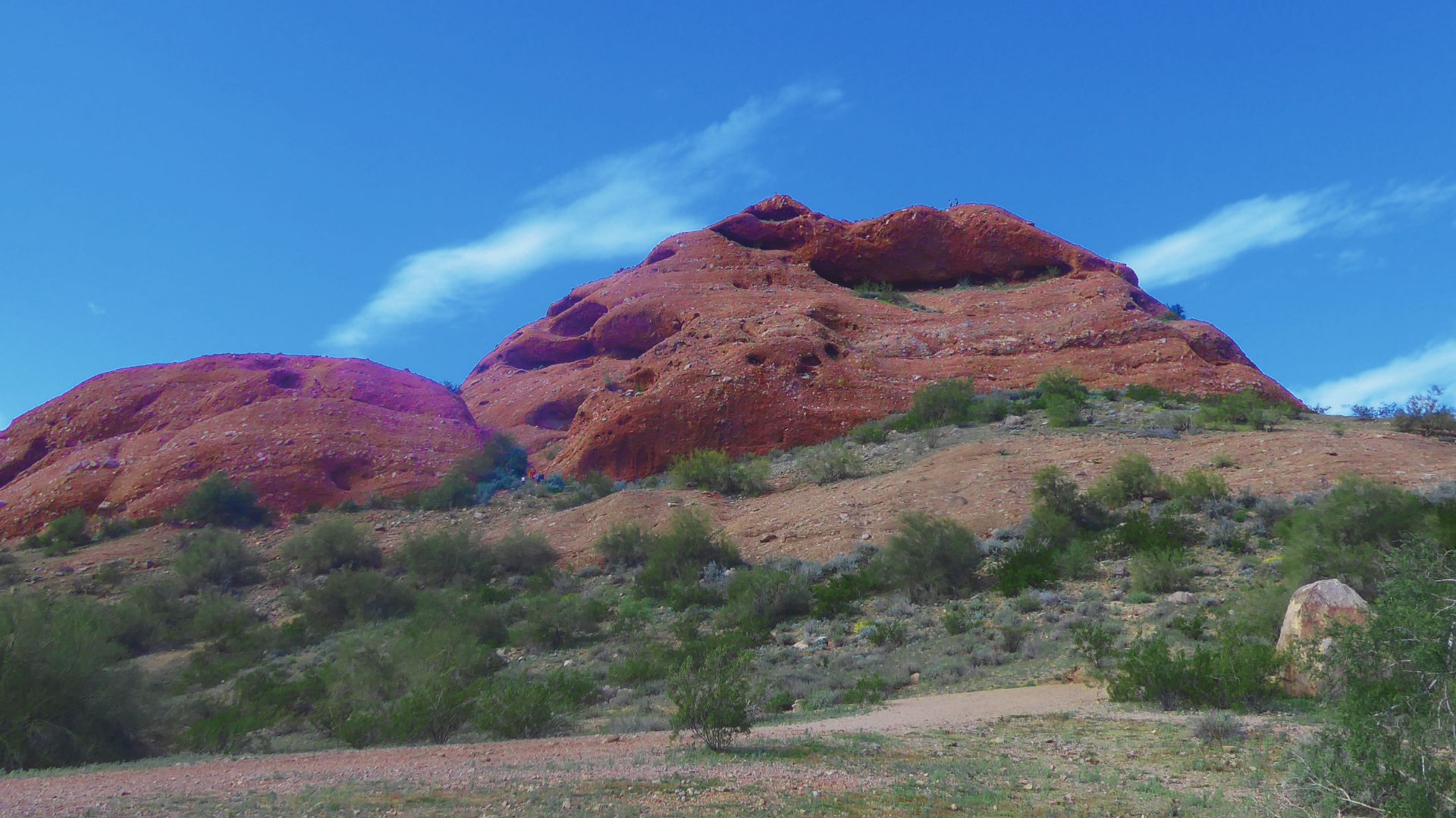A dramatic red rock formation stands prominently, highlighting its unique shape and rich, warm hues under sunlight.