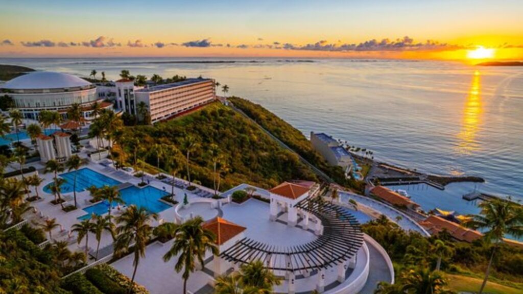 A vibrant sunset casts warm hues over the Caribbean ocean and a luxurious resort, creating a serene tropical scene.