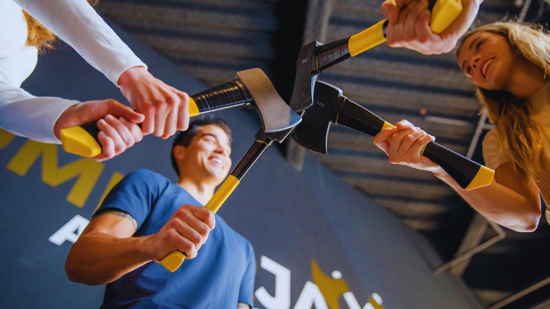 Three individuals hold a hammer in front of a sign, showcasing teamwork and readiness for a construction project.