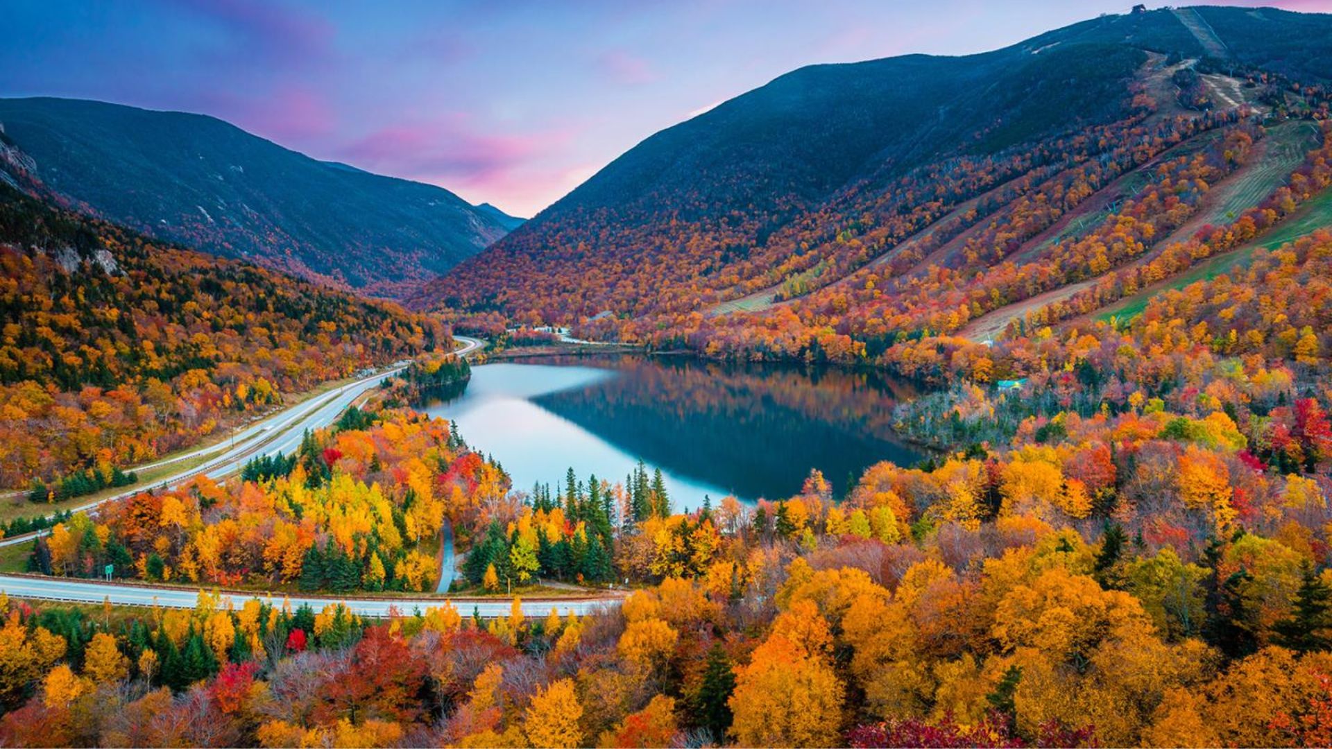 Vibrant fall foliage blankets the mountains, showcasing a stunning array of red, orange, and yellow leaves.