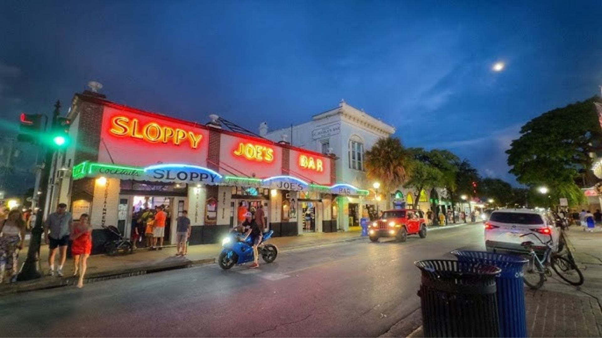 A vibrant street scene featuring a neon sign that reads "Slowey's," illuminating the surroundings with colorful light.