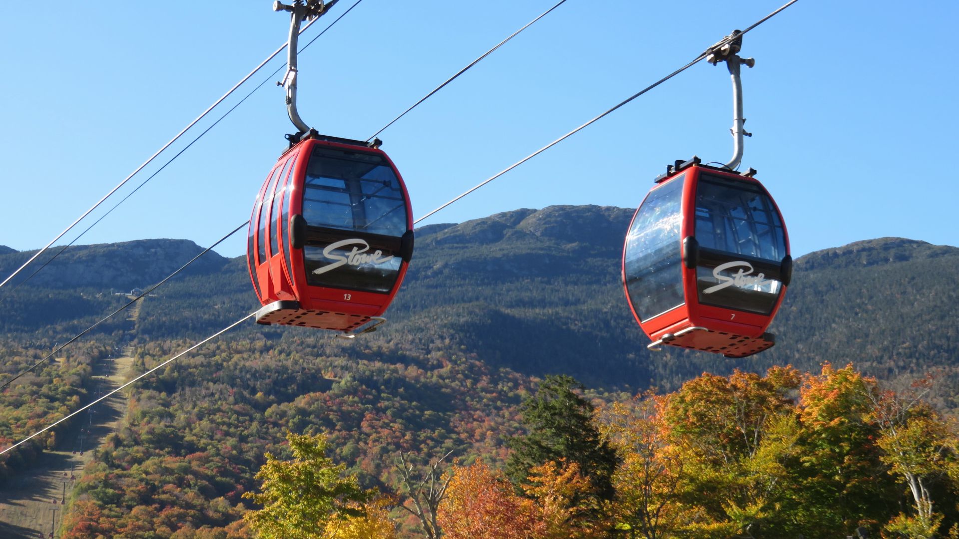 Two gondolas glide above a scenic mountain landscape, showcasing the beauty of the surrounding peaks.