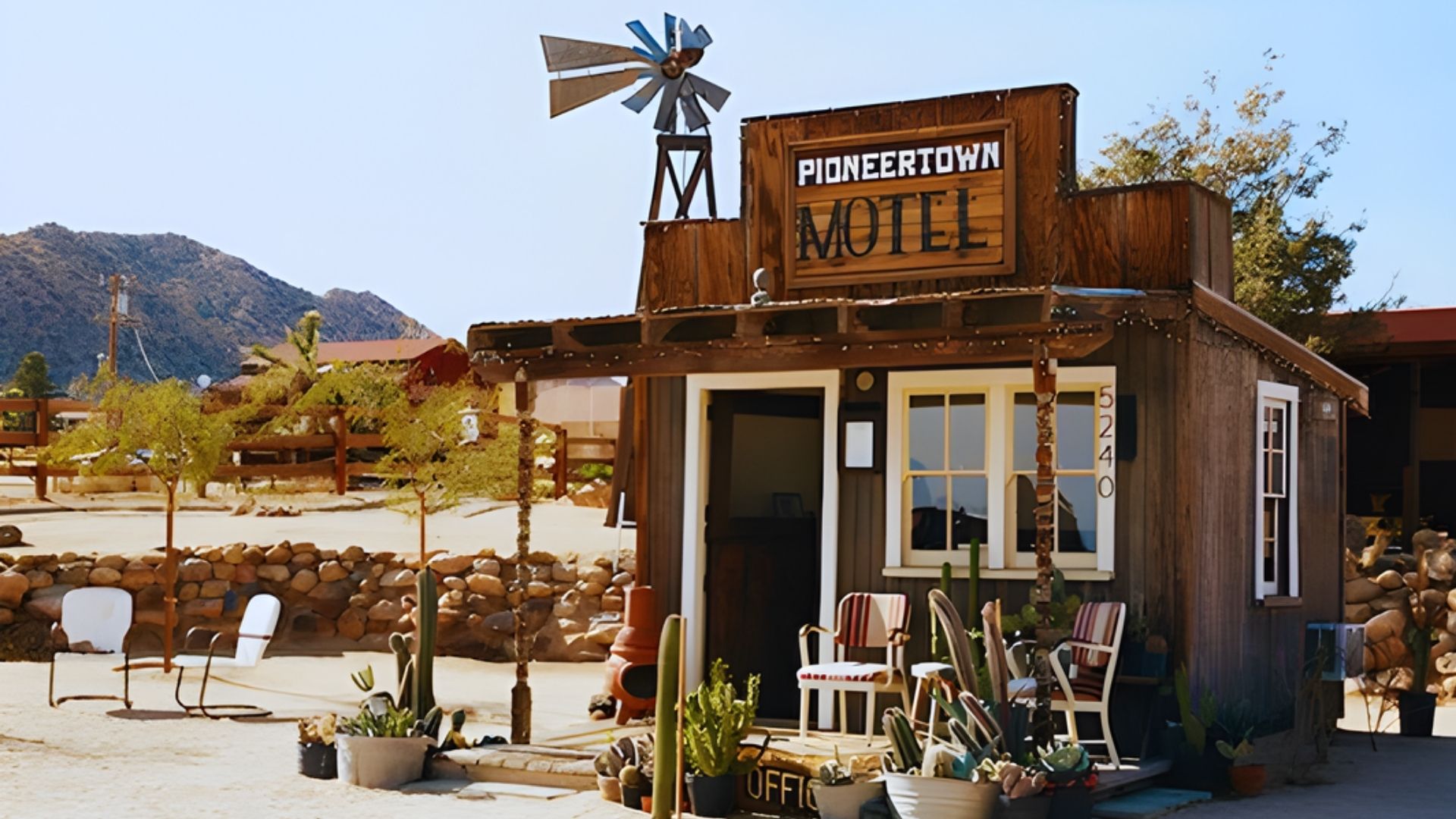 A small building beside a windmill, surrounded by several cactus plants under a clear blue sky.