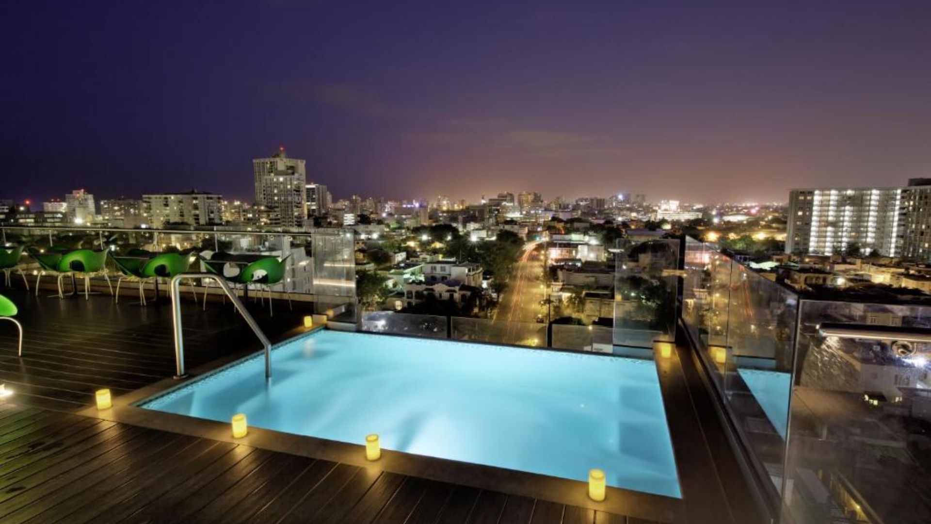 A rooftop pool illuminated at night, offering a stunning view of the city skyline and twinkling lights below.
