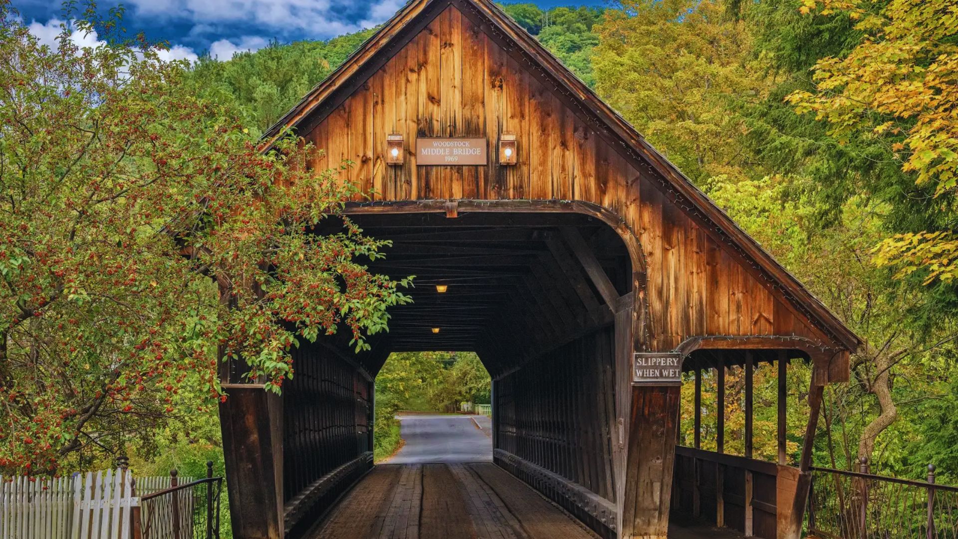 A scenic view of a covered bridge nestled in the mountains of New York, surrounded by lush greenery and blue skies.