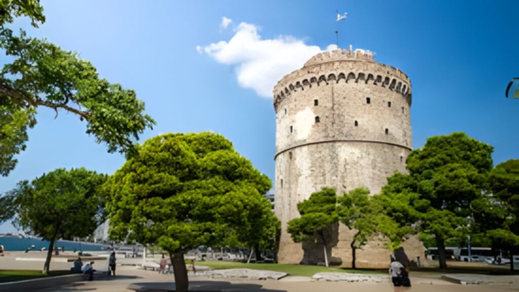 The White Tower in Athens, Greece, a historic round stone structure surrounded by greenery and blue sky.