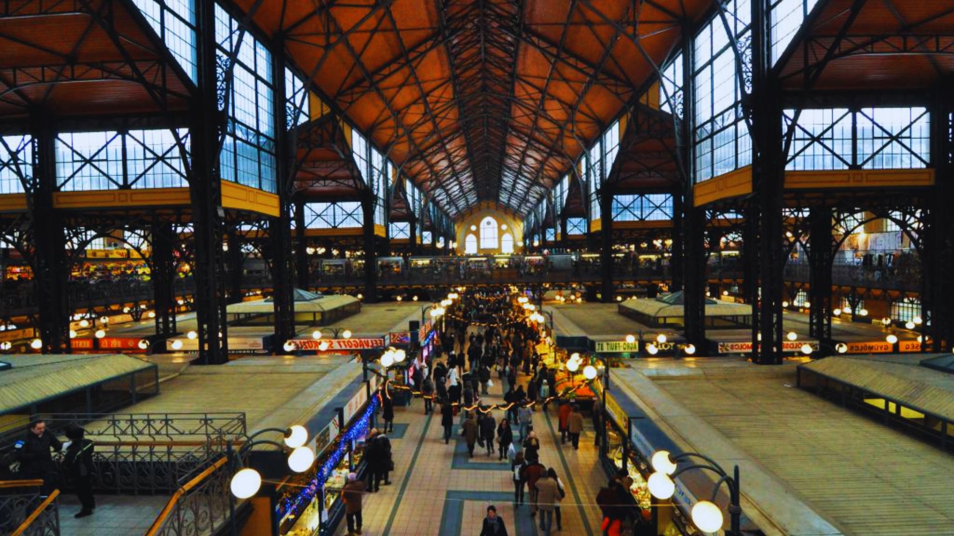 A bustling indoor market filled with numerous people shopping and exploring various stalls and products.