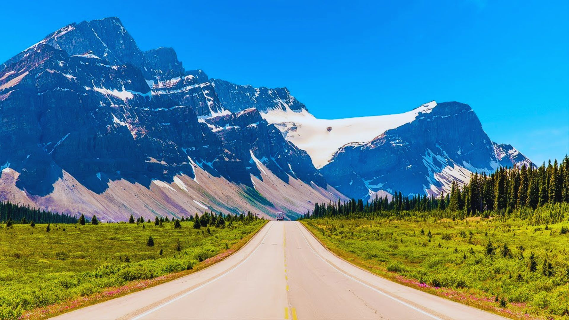 A winding road stretches towards a distant mountain range under a clear blue sky.
