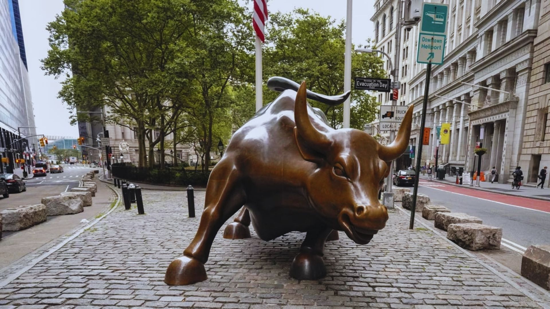 A bronze bull statue stands on the street in front of a building, showcasing its detailed features and strong presence.