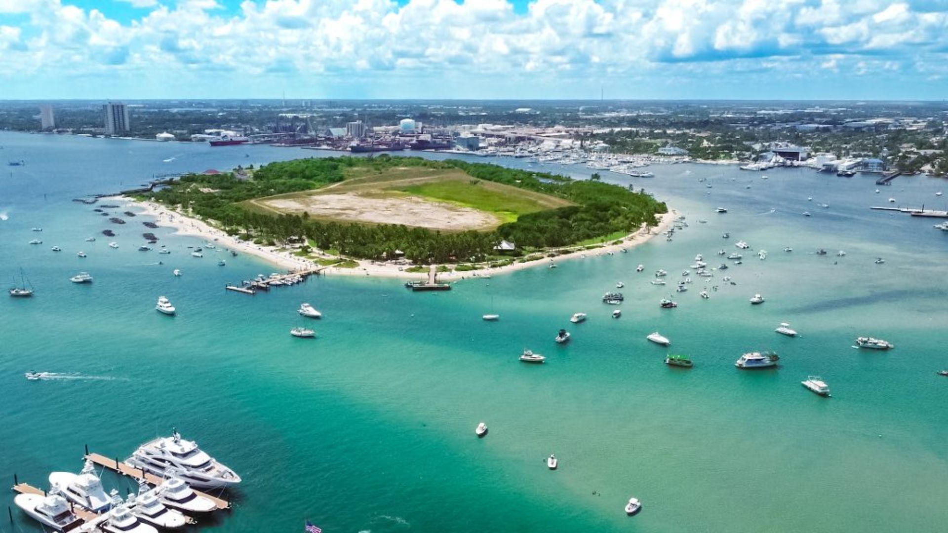 Aerial view of a lush green island surrounded by blue water, with several boats scattered in the bay.