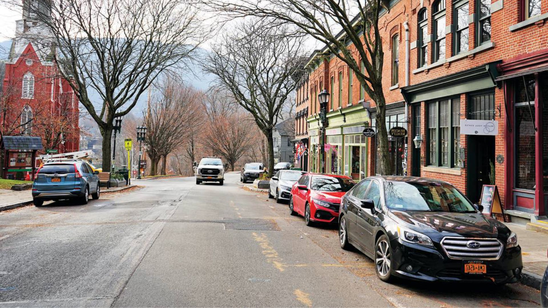 A street lined with parked cars and buildings on both sides, showcasing urban architecture and everyday city life.