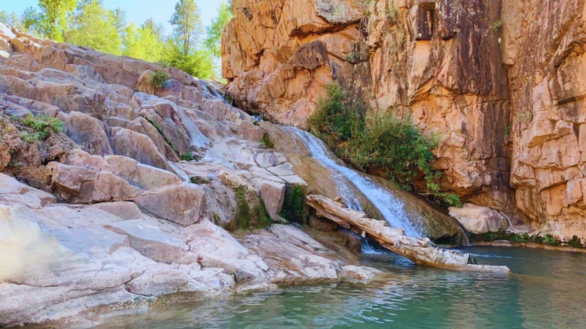 A cascading waterfall flows through a narrow canyon, surrounded by rugged rock formations and lush greenery.