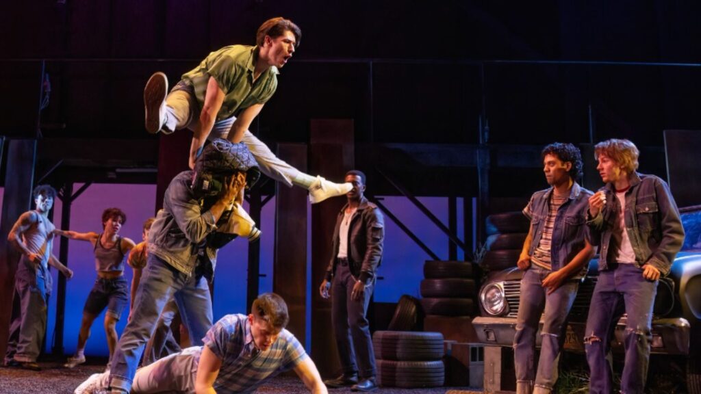 The cast of the stage show Grease poses together, showcasing their vibrant costumes and energetic expressions.